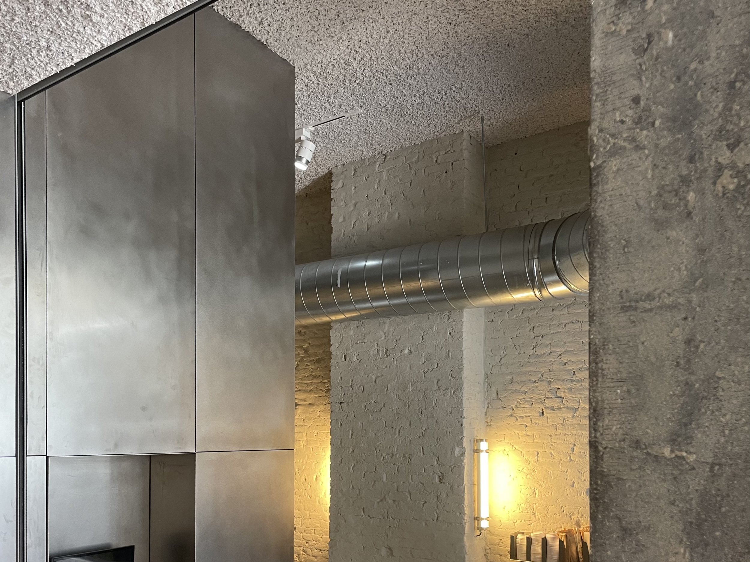 Modern interior space with gray cabinets, exposed brick walls, a concrete surface, and metallic industrial air ducts, illuminated with warm lighting.