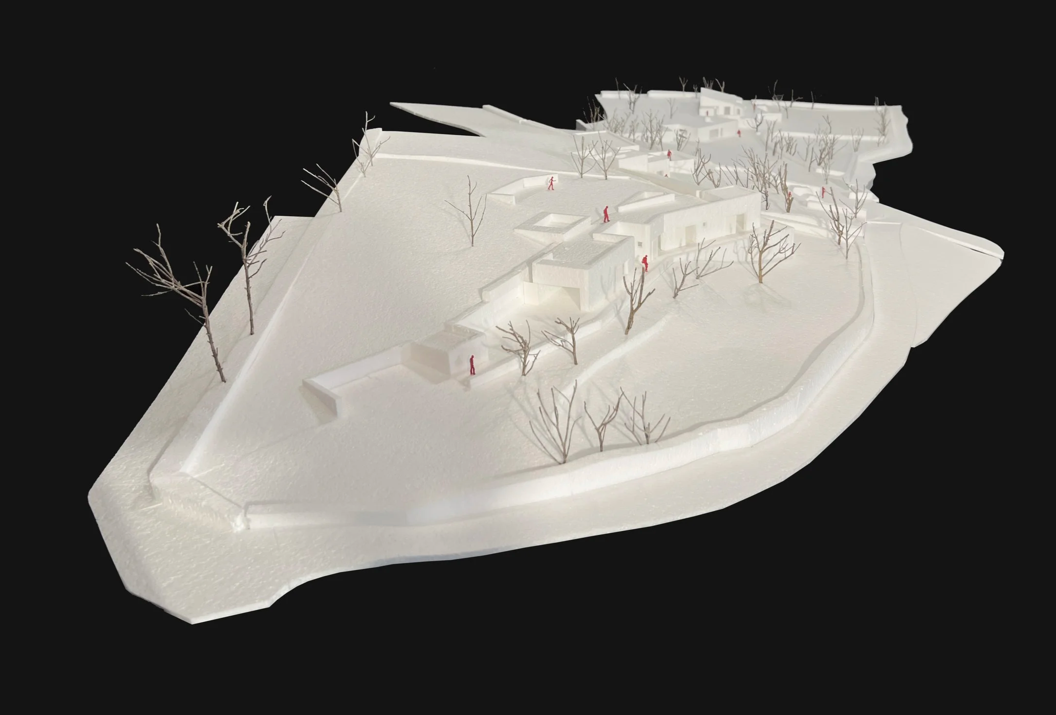 White architectural model of a hillside residential area with leafless trees and small human figures, set against a black background.
