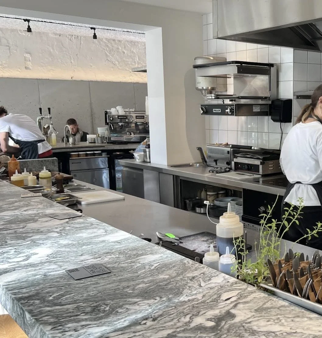 A modern restaurant kitchen with a marble countertop, cooking utensils, condiments, and professional kitchen appliances, with chefs preparing food in the background.