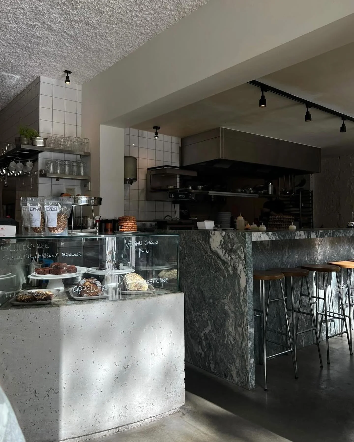 Interior of a modern cafe with baked goods on display, marble counter, and high stools at a bar