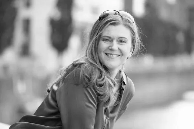 Schwarz-weiß-Fotografie einer lachenden Frau mit langen Haaren die im Freien sitzt.