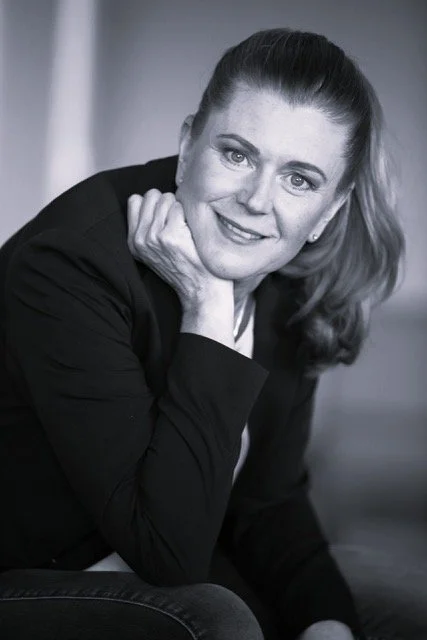 Schwarz-weiß Portrait einer lächelnden Frau mit langen Haaren, die eine Hand an das Kinn hält.