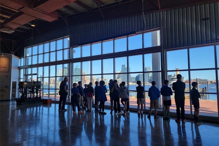 Children and adults looking out large window of building at city skyline and water.