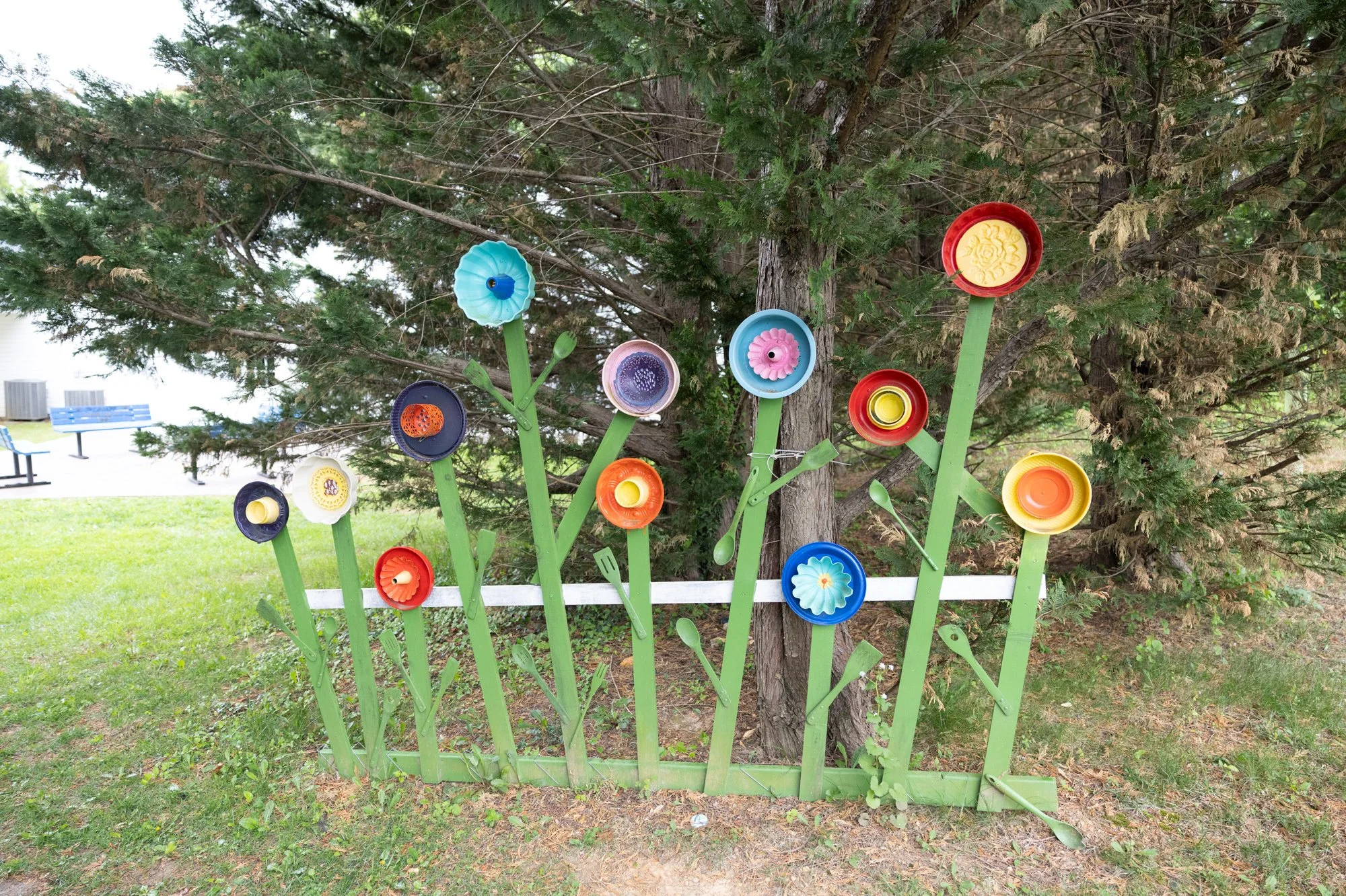 Colorful flower-shaped cups attached to green stems in front of a tree in a park.