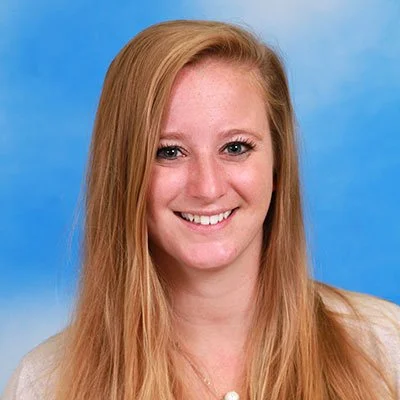 A young woman with long red hair smiling against a blue background.