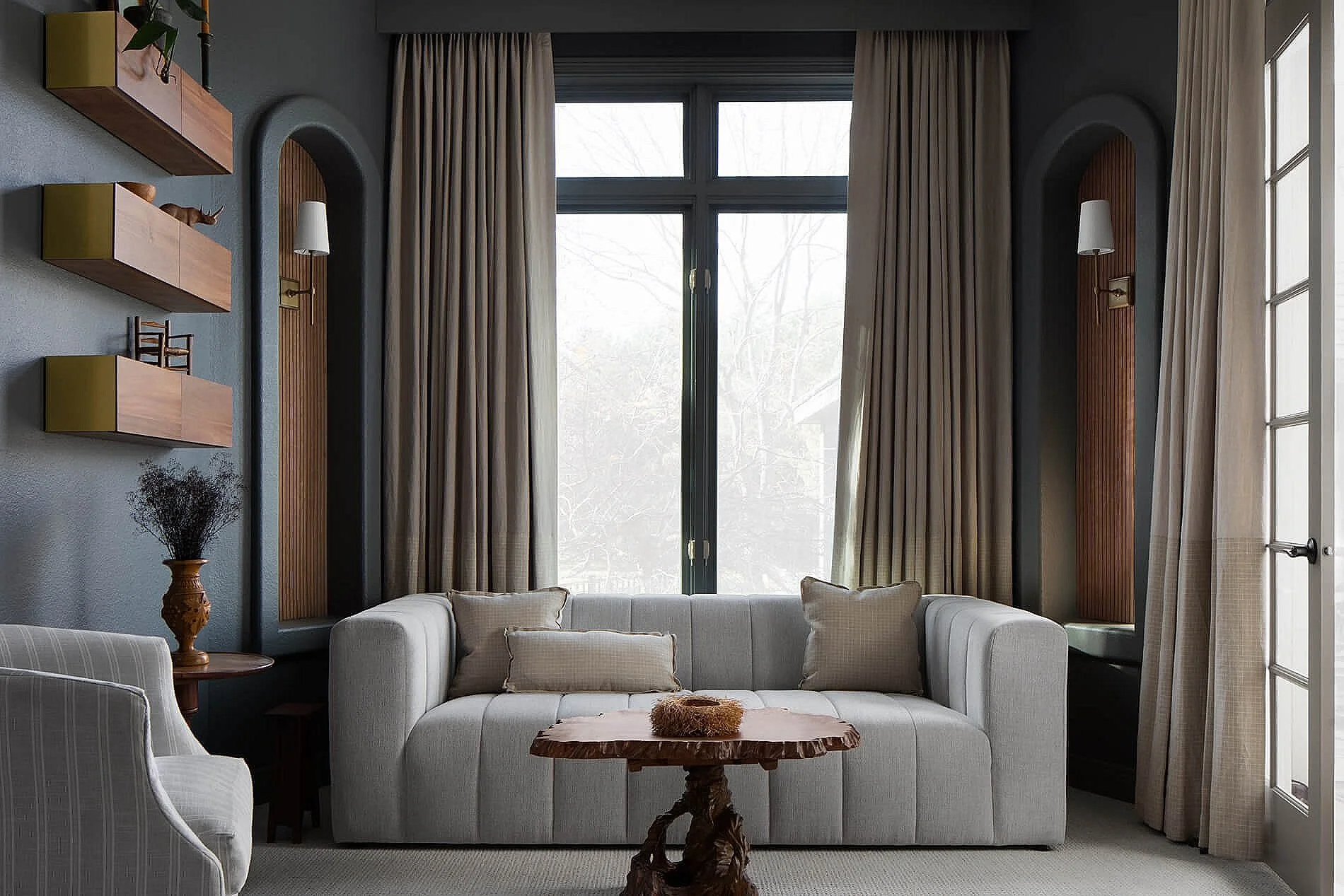 Elegant living room with white sofa, wood coffee table, arched wall niches, shelving, and tall curtained windows