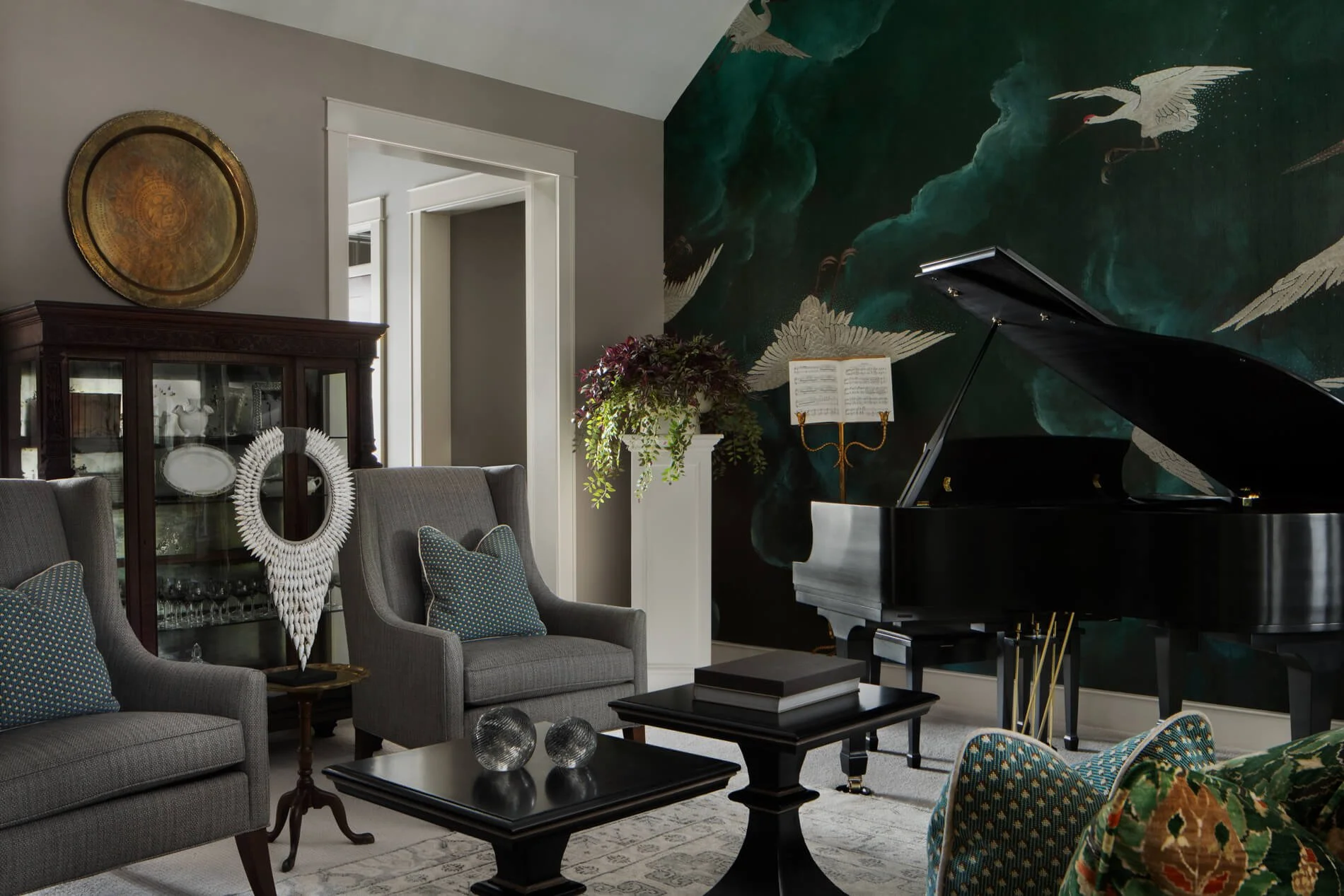 Elegant living room with a black grand piano, bird mural wallpaper, gray armchairs, glass-front cabinet, and coffee tables