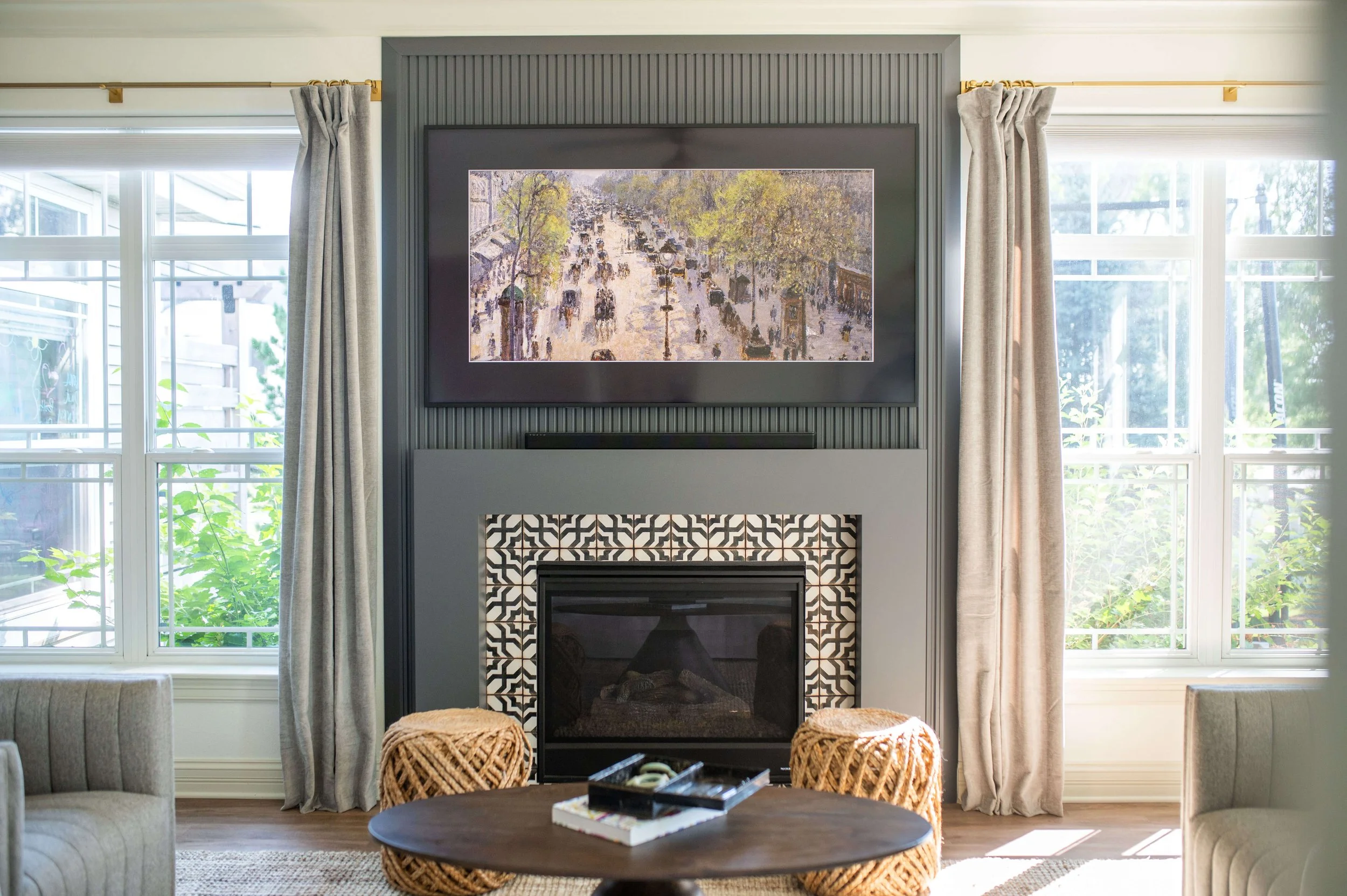 Living room with a fireplace, large windows with curtains, and a painting above the mantel.