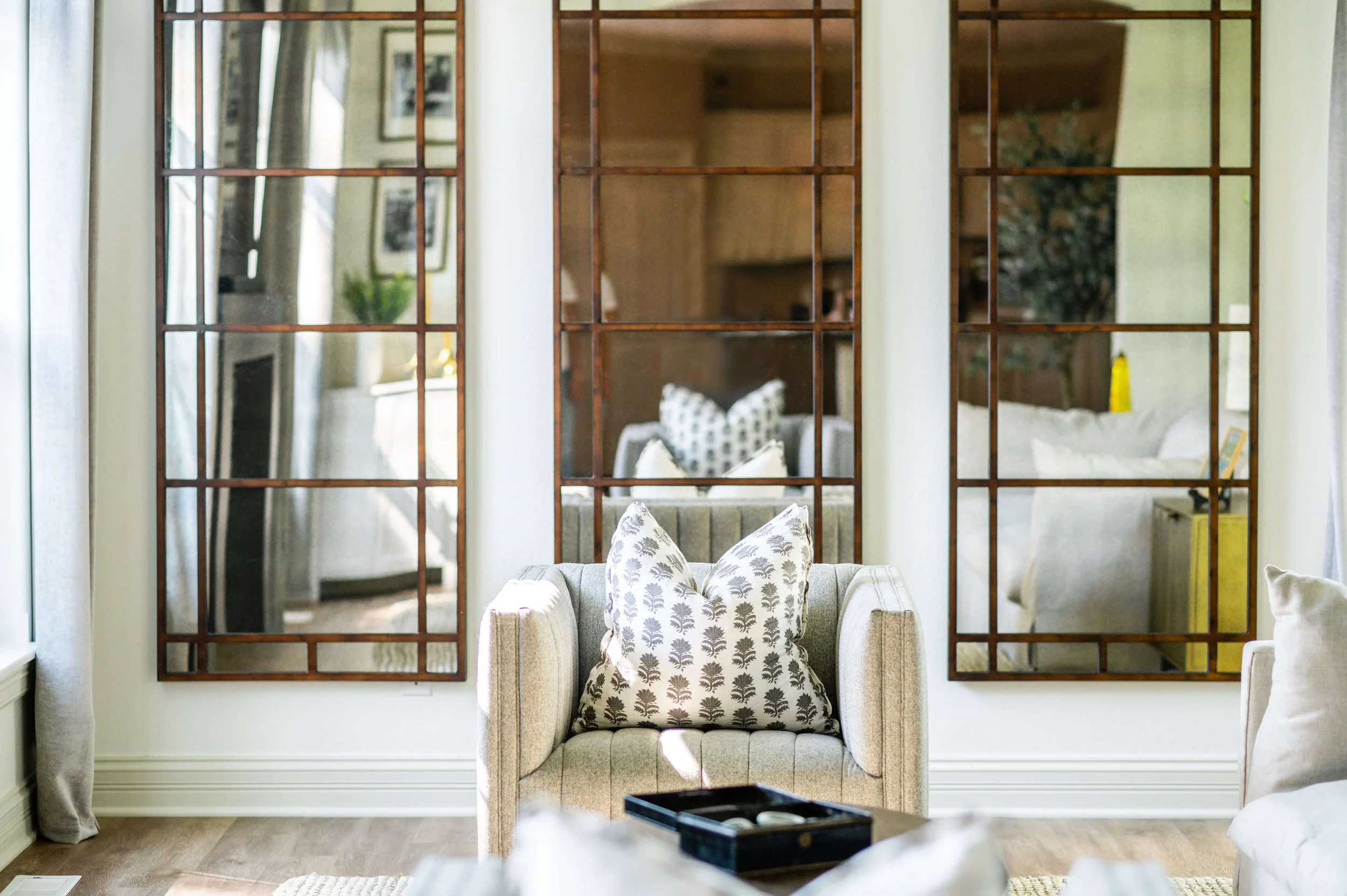 Decorative wall mirror with grid pattern reflecting cozy living room with armchairs and pillows.