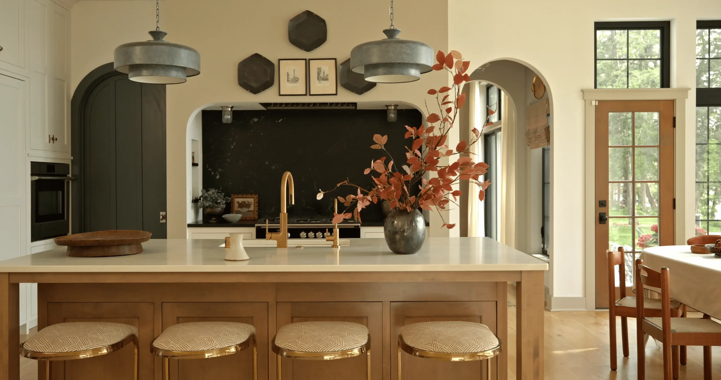 Elegant modern kitchen with a large island, brass fixtures, black marble backsplash, pendant lights, and autumn branches in a vase