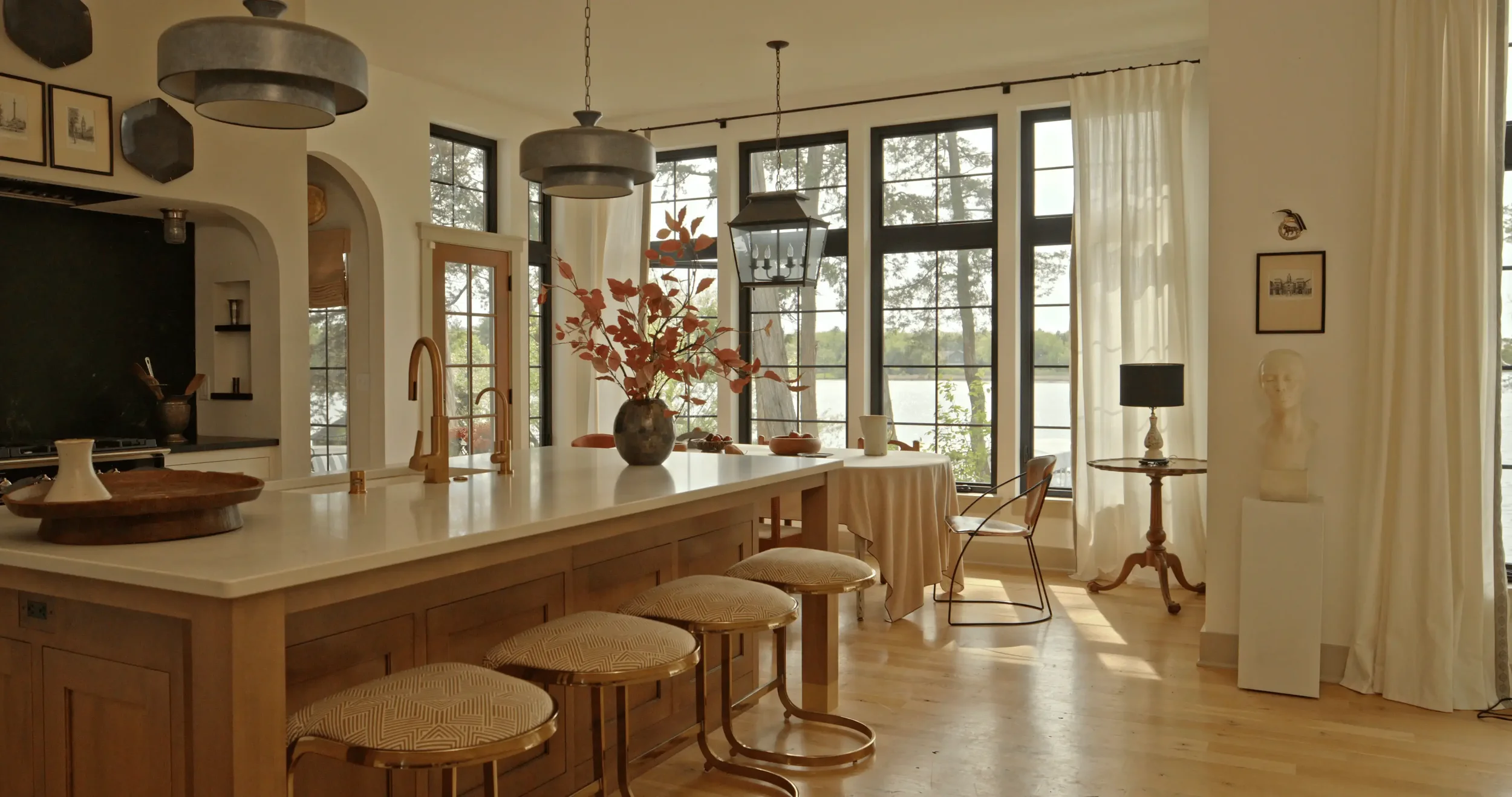Elegant modern kitchen and dining area with a large island, pendant lights, black-framed windows, and lake views