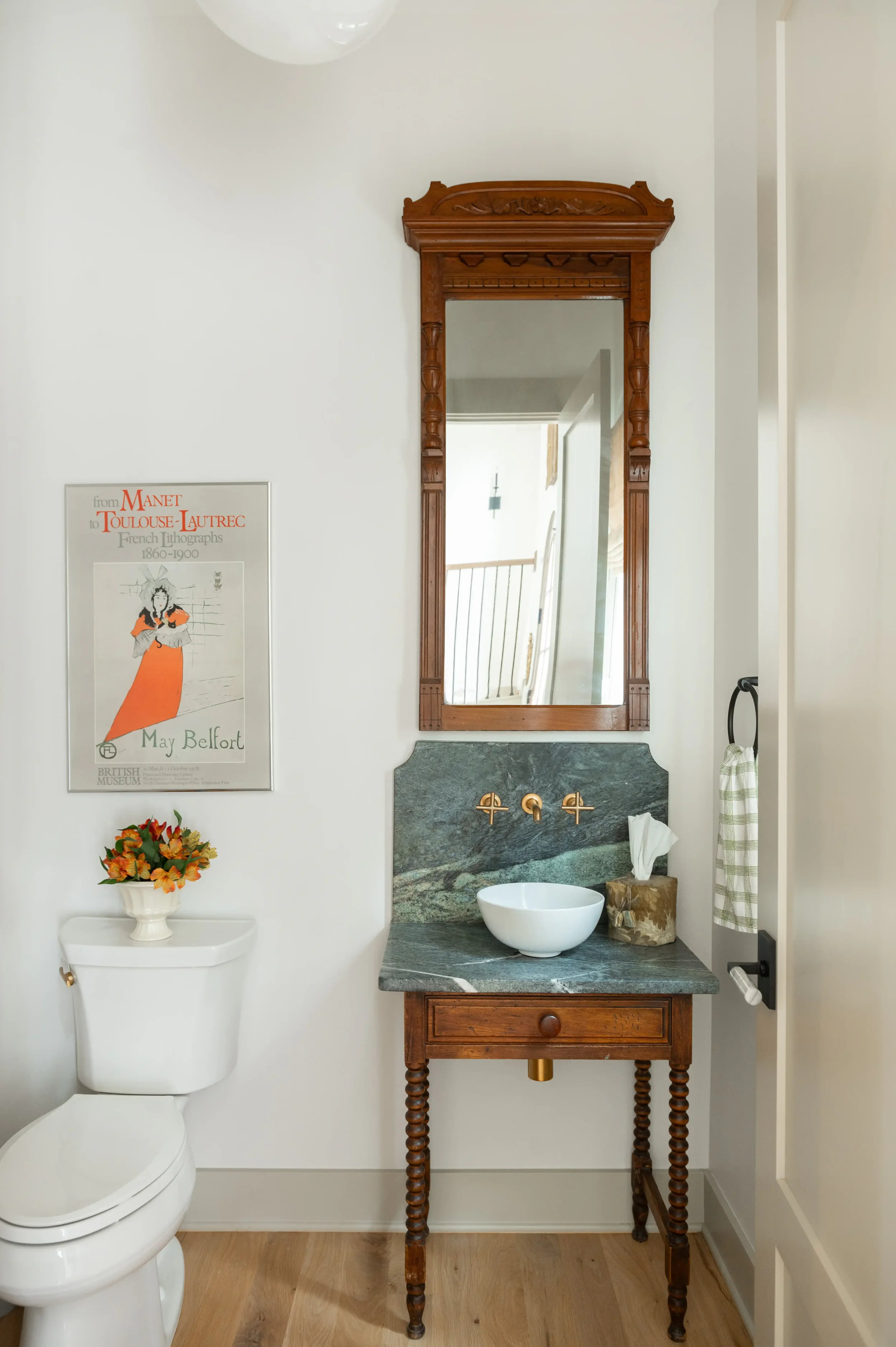 Elegant bathroom with an ornate wood-framed mirror, marble vanity, vessel sink, toilet, framed art, and flowers