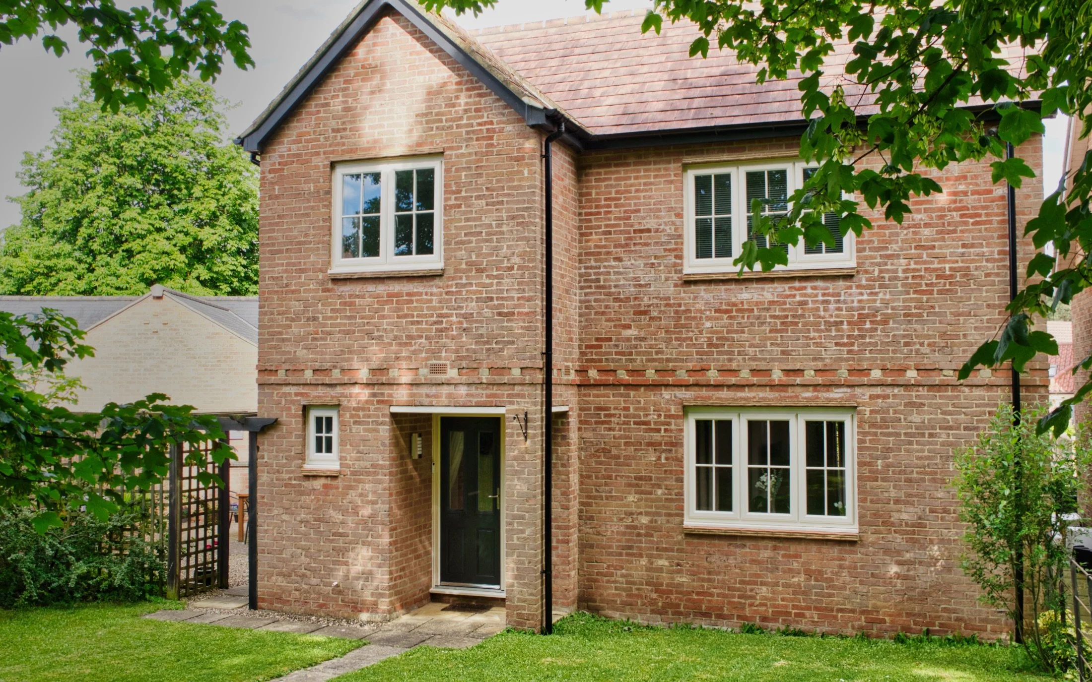 An example photo of the exterior of a detached house, surrounded by a lawn and trees.