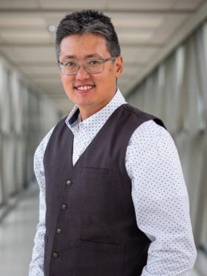Portrait of Michael Chan standing in a corridor wearing a black vest, 