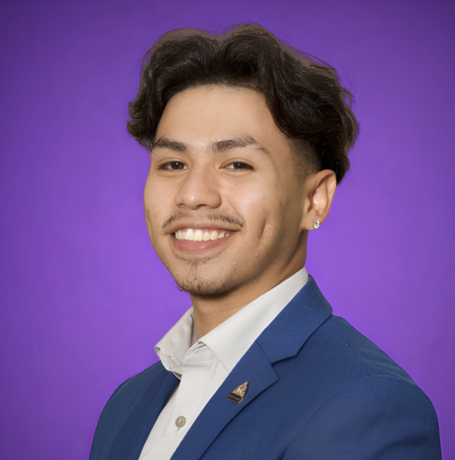 Portrait of Jose Perez smiling against a bright-purple background wearing a blue suit.