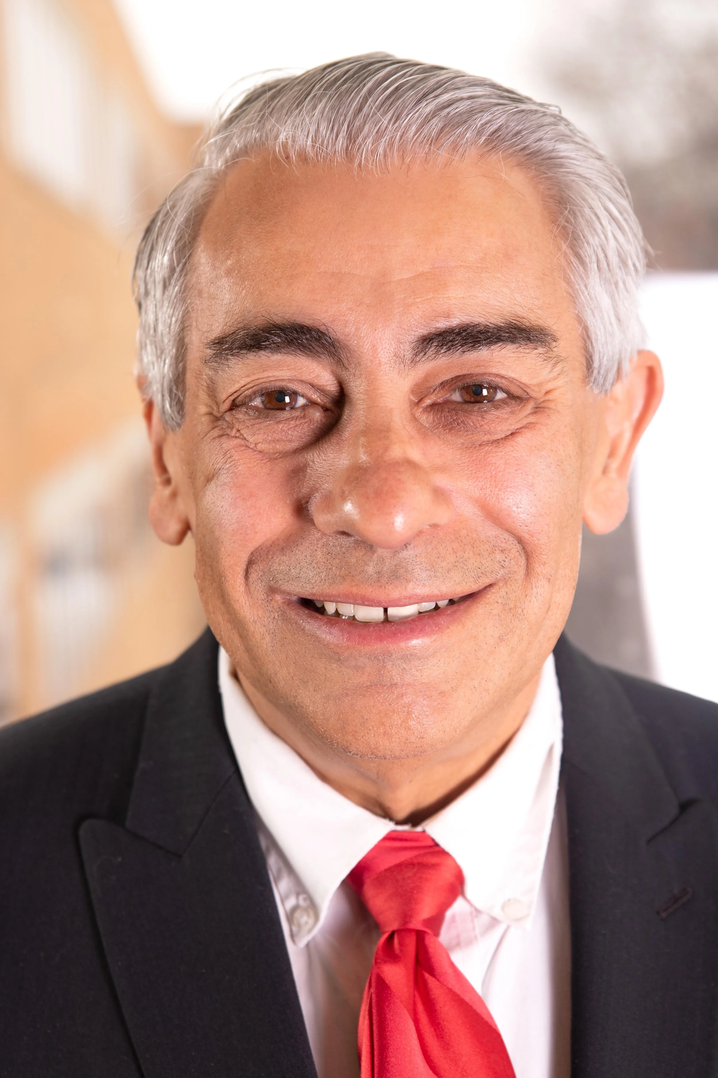 Portrait of King Banaian smiling in a black suit and red tie.