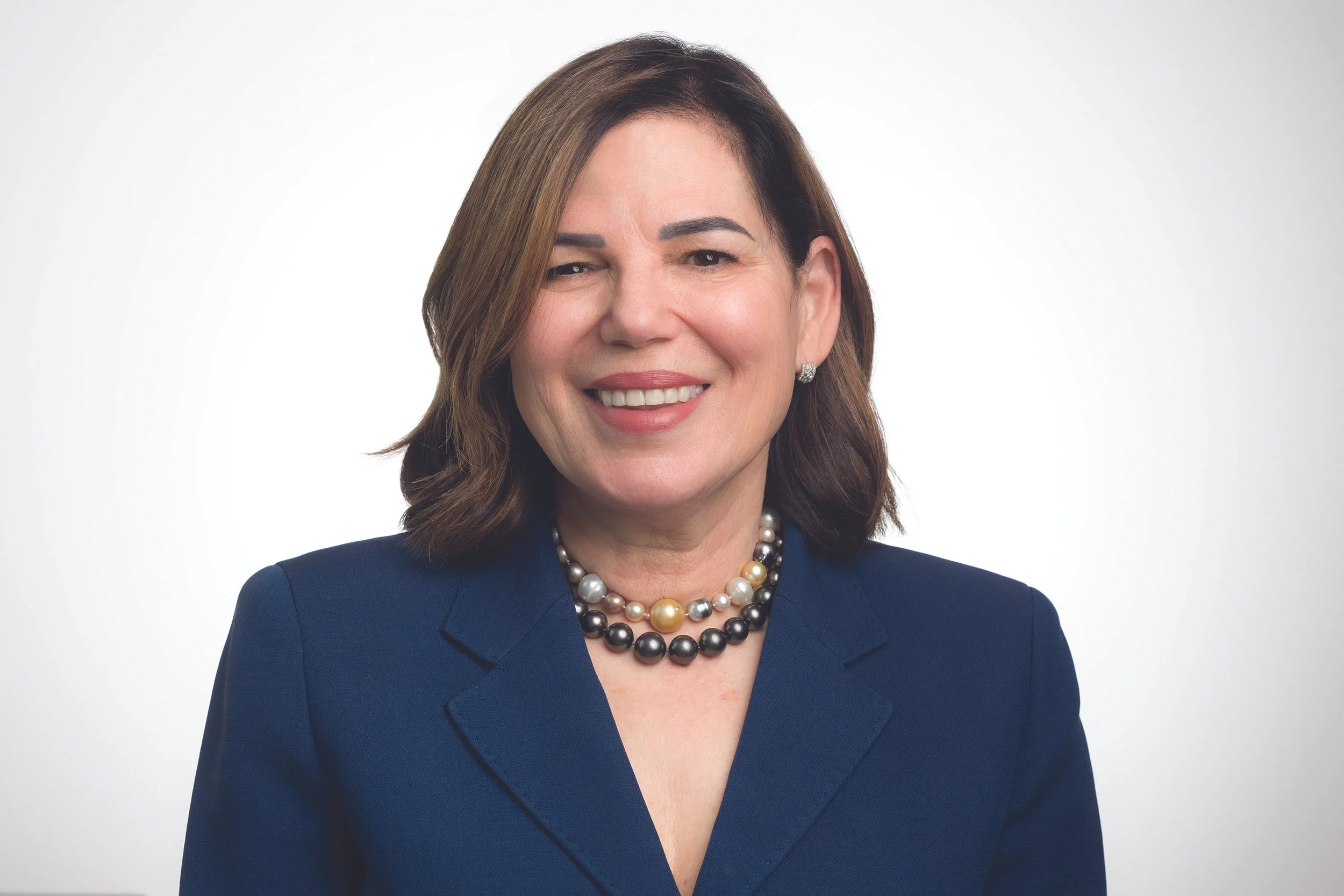 Portrait of Rabbi Marcia Zimmerman with brown hair, wearing a navy blazer, pearl necklace, and earrings.