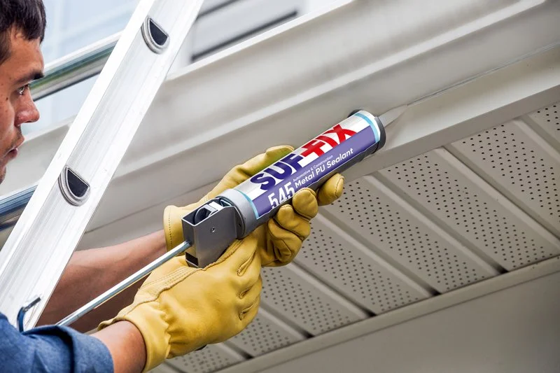 Person wearing yellow gloves applying sealant under an attic roof.