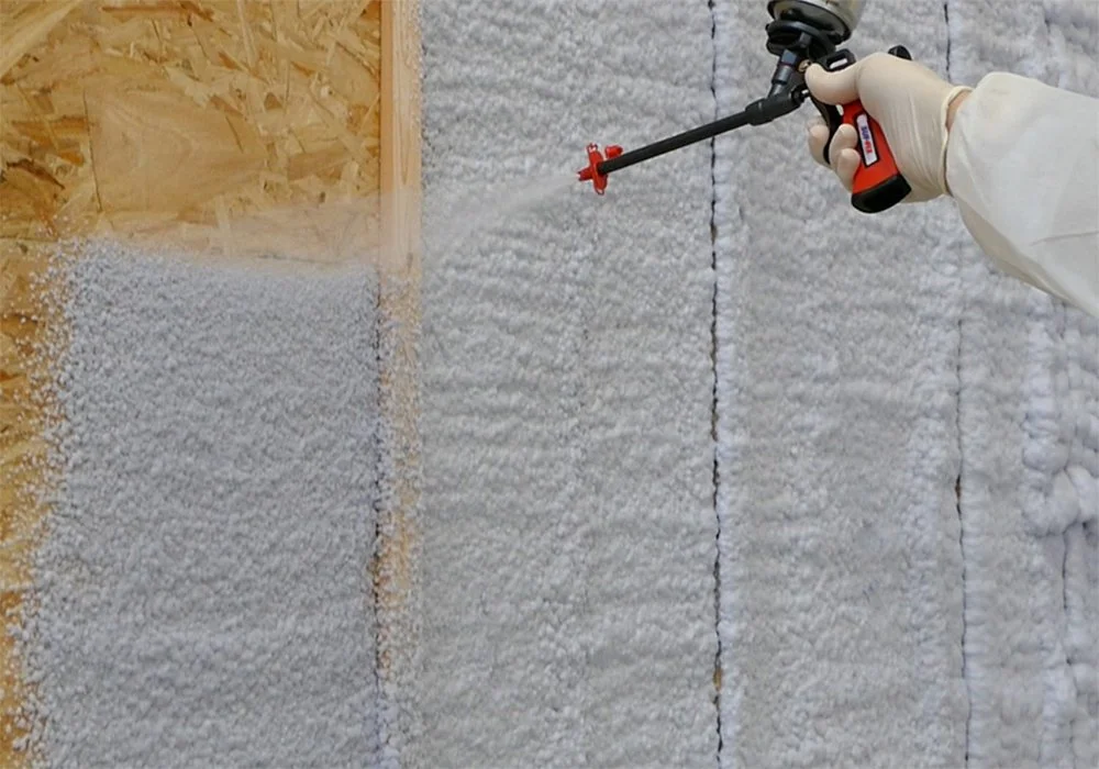 Someone wearing gloves sanitizing or disinfecting a wall with spray foam insulation using a handheld sprayer.
