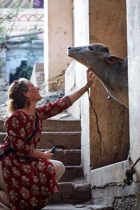 Une femme en robe rouge avec des motifs touche doucement le museau d'un éléphant dans un bâtiment en pierre.