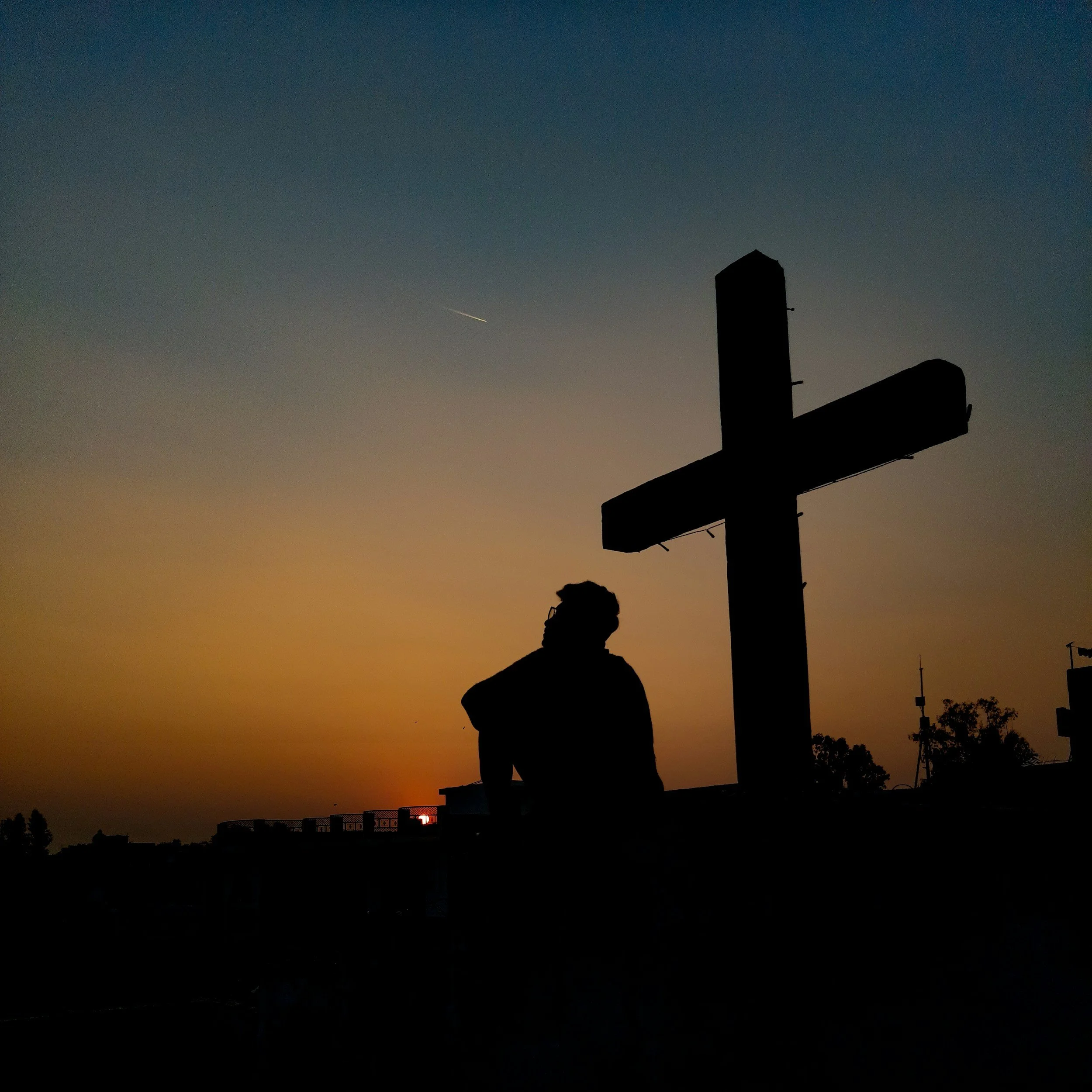 Silhouette of a person standing outdoors during sunset with a sunset sky in the background, and a street sign on the right side of the image.