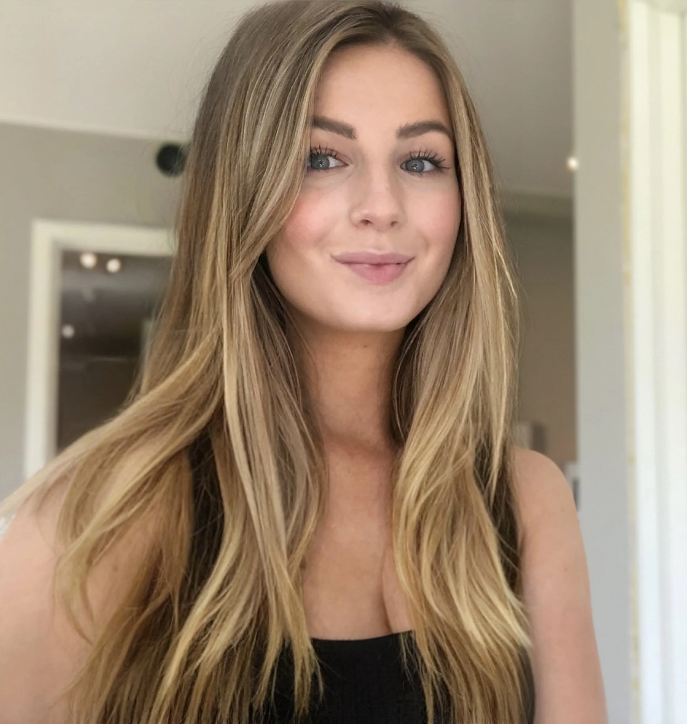 Et nærbilde av en smilende kvinne med langt, blond hår og blå øyne i et innendørs miljø.