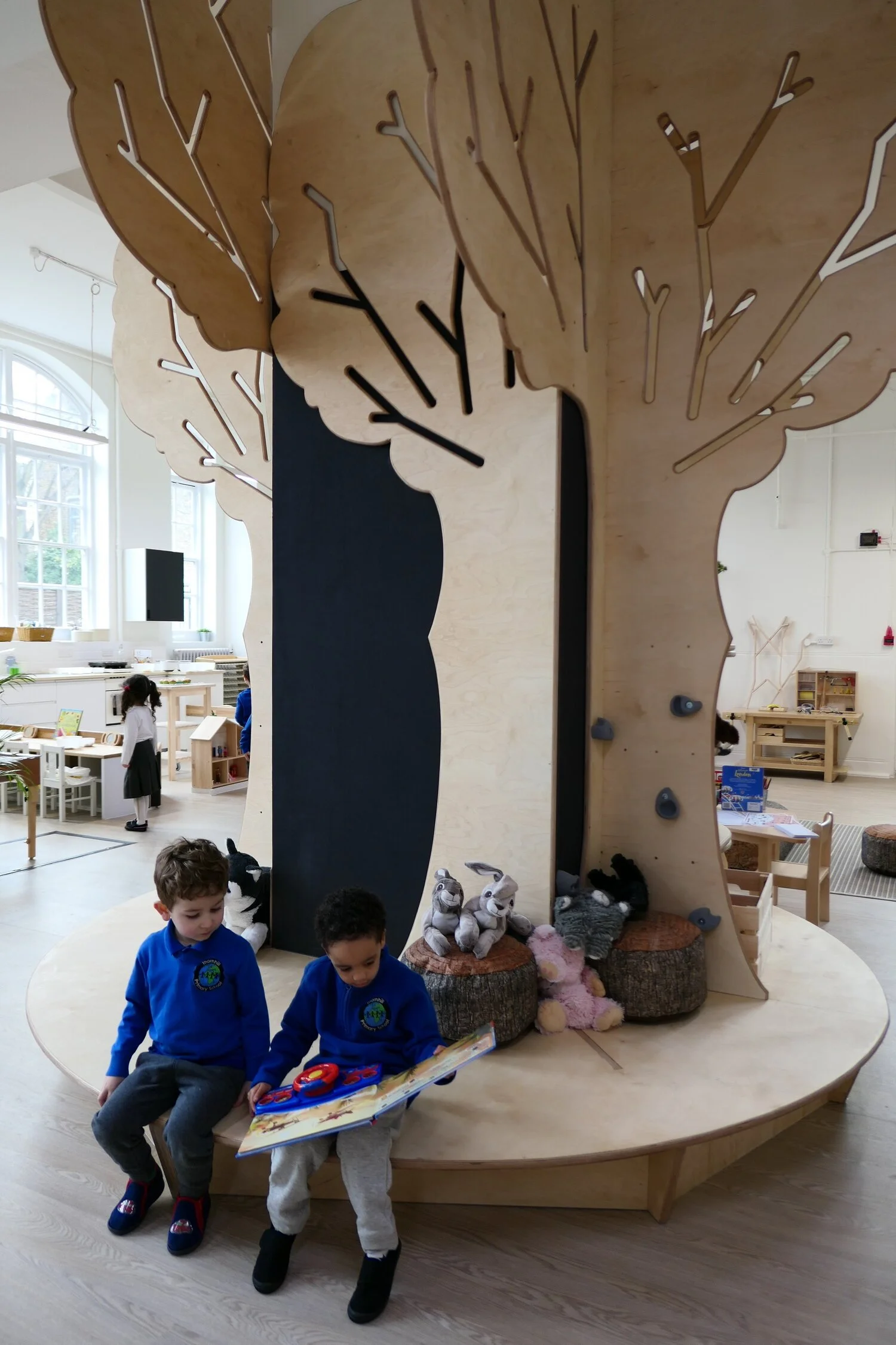 Children sitting around a bespoke, custom made decorative tree out of birch ply