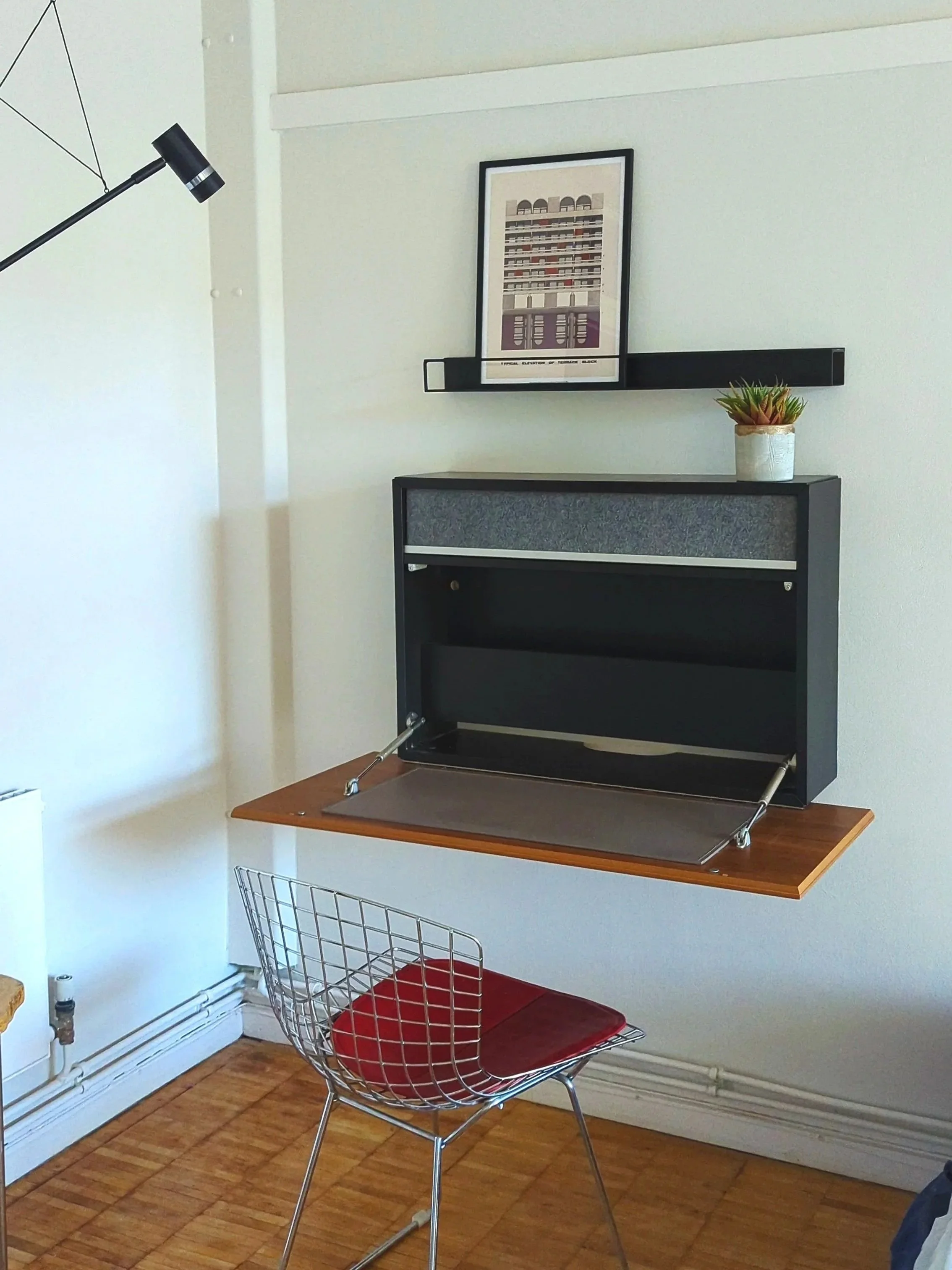 Midcentury modern wire chair with a wall hung drop down desk, a print of the barbican sits nicely on the shelf above. 