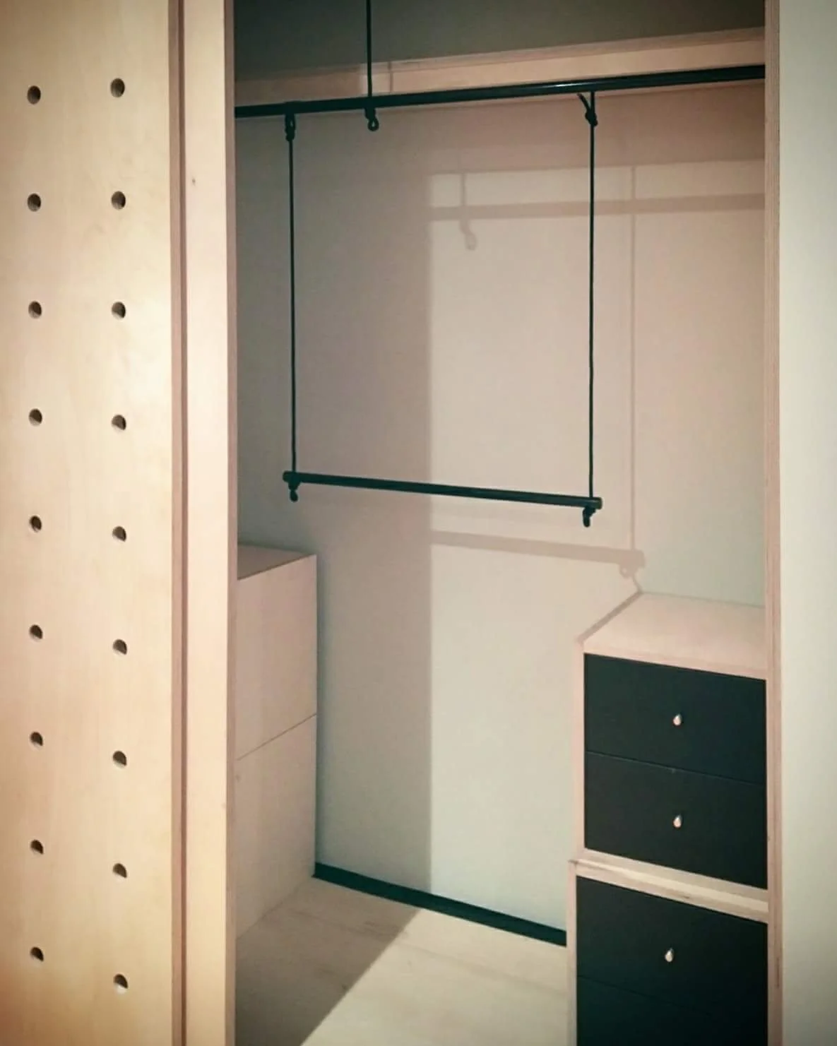 bespoke closet sliding doors with partially assembled wooden frame, black drawers, and a hanging rod suspended by ropes.