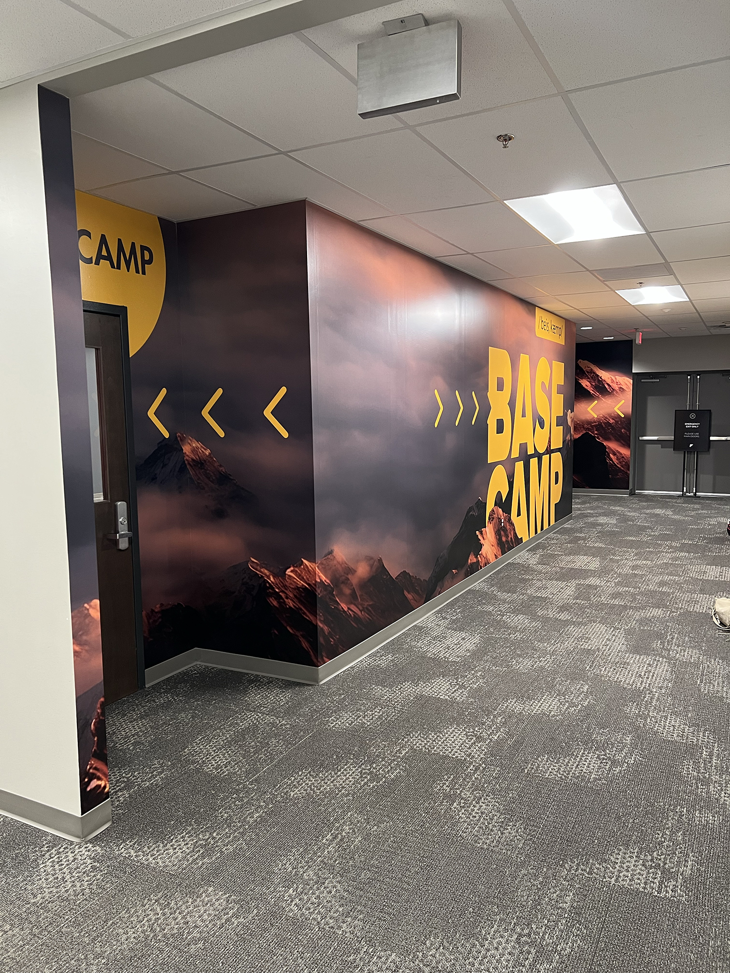 Hallway wall with mountain landscape poster and yellow text reading "BASE CAMP" with yellow arrows pointing right.