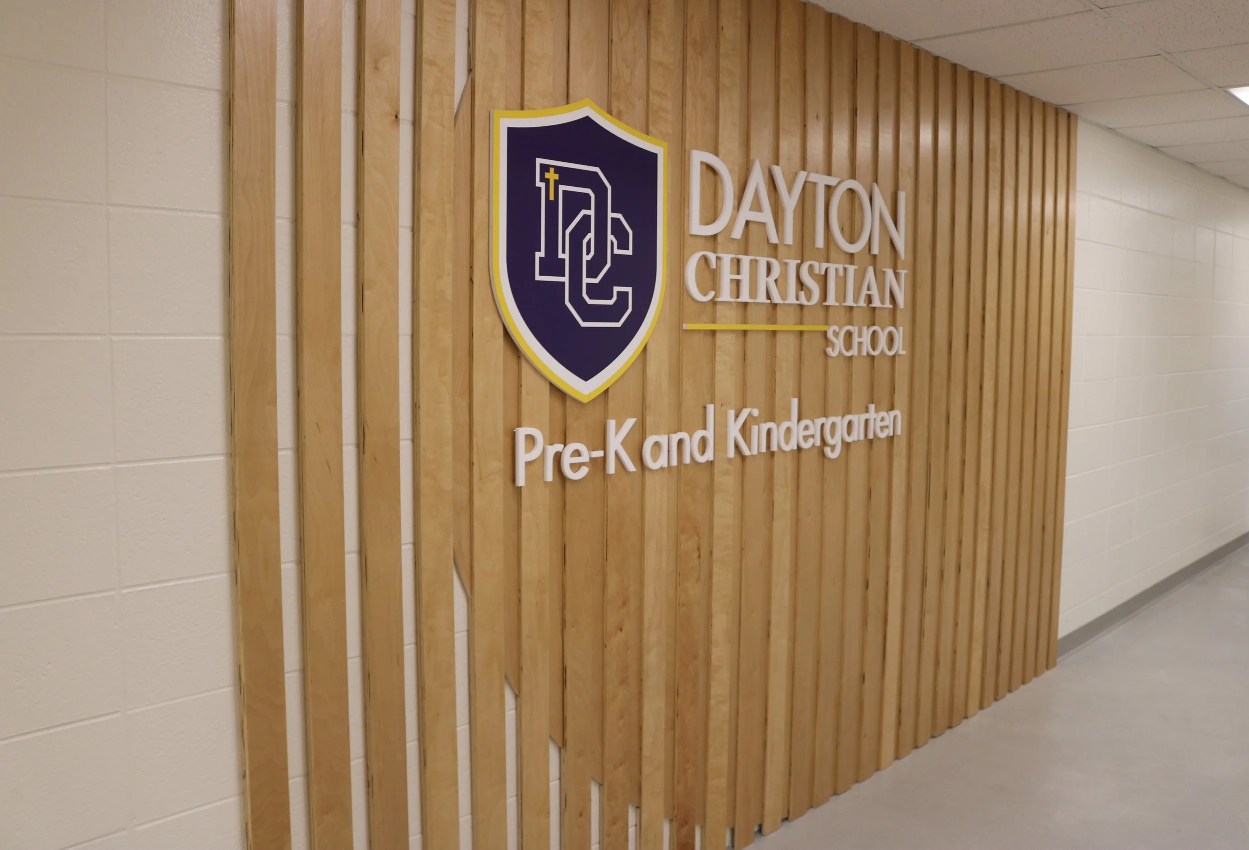 Interior hallway of Dayton Christian School featuring a wooden wall with the school's logo and name, with the words 'Pre-K and Kindergarten' displayed underneath.