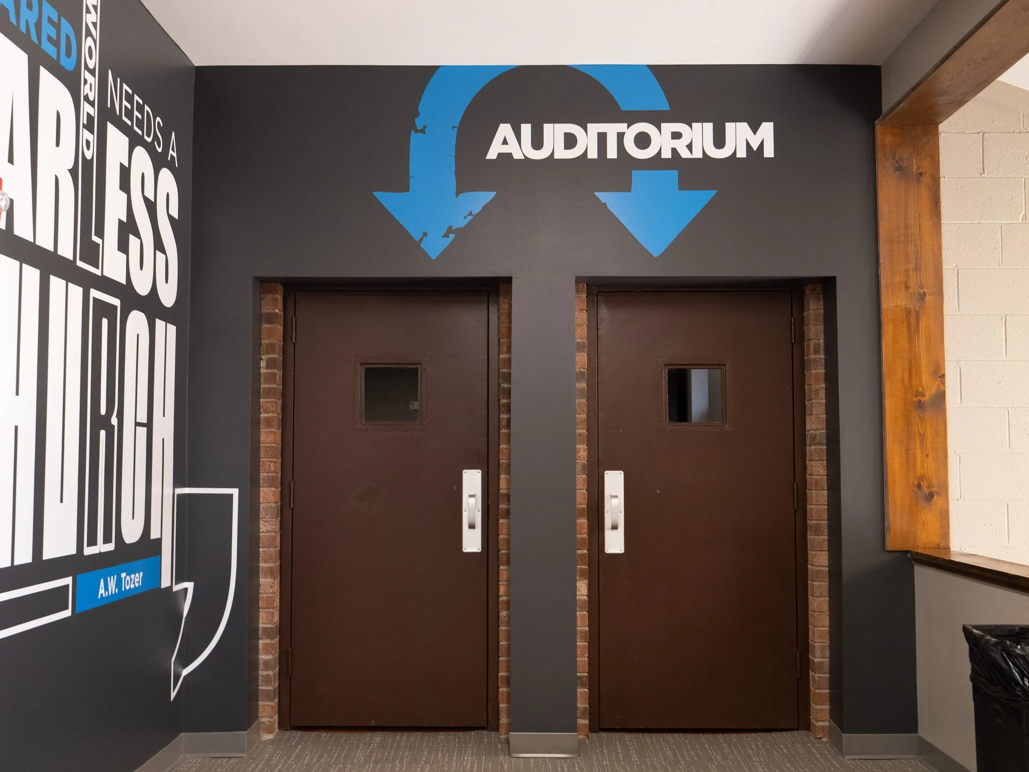 Double doors to an auditorium with a sign above. The sign has two blue arrows pointing down and the word 'Auditorium' in white letters.