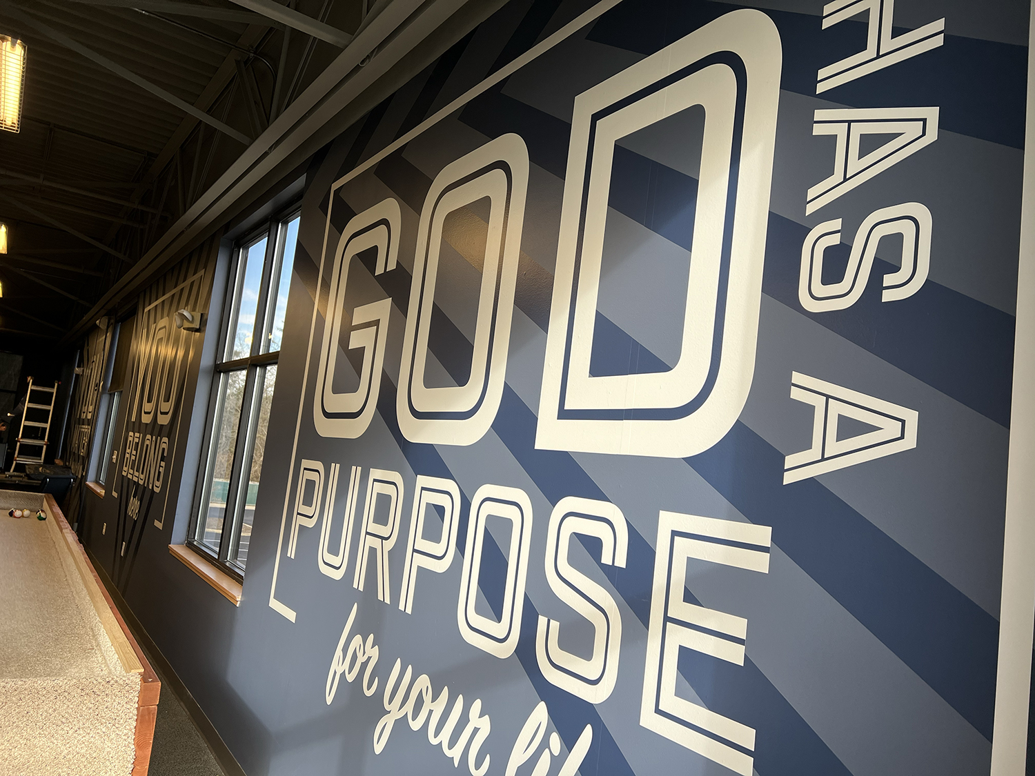 Indoor golf training center featuring a large wall mural with the text "GOD PURPOSE for your life" and a pool table.