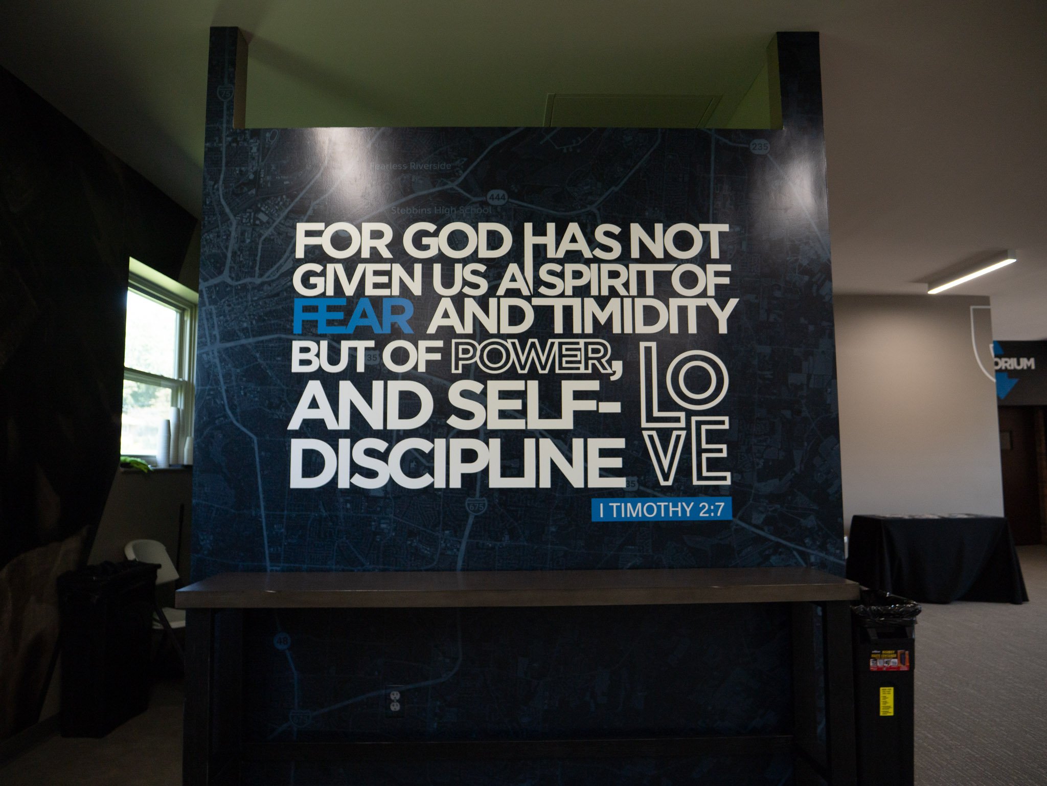 A large vertical display with a dark blue background featuring a map and the biblical quote from 1 Timothy 2:7 in bold white and blue letters, reading "For God has not given us a spirit of fear and timidity but of power, love, and self-discipline."