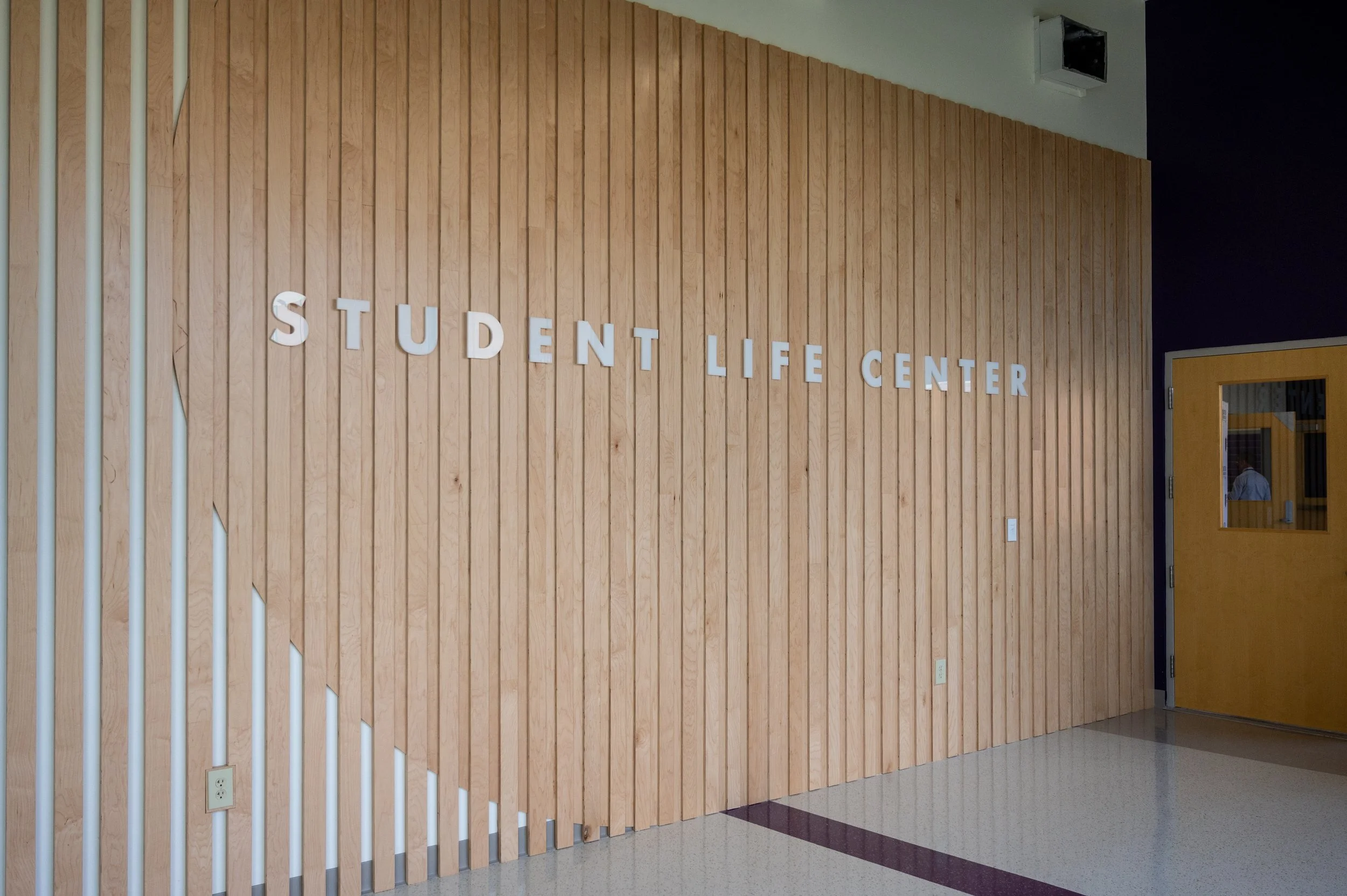 Wood-paneled wall with white letters spelling "STUDENT LIFE CENTER" in a school hallway.