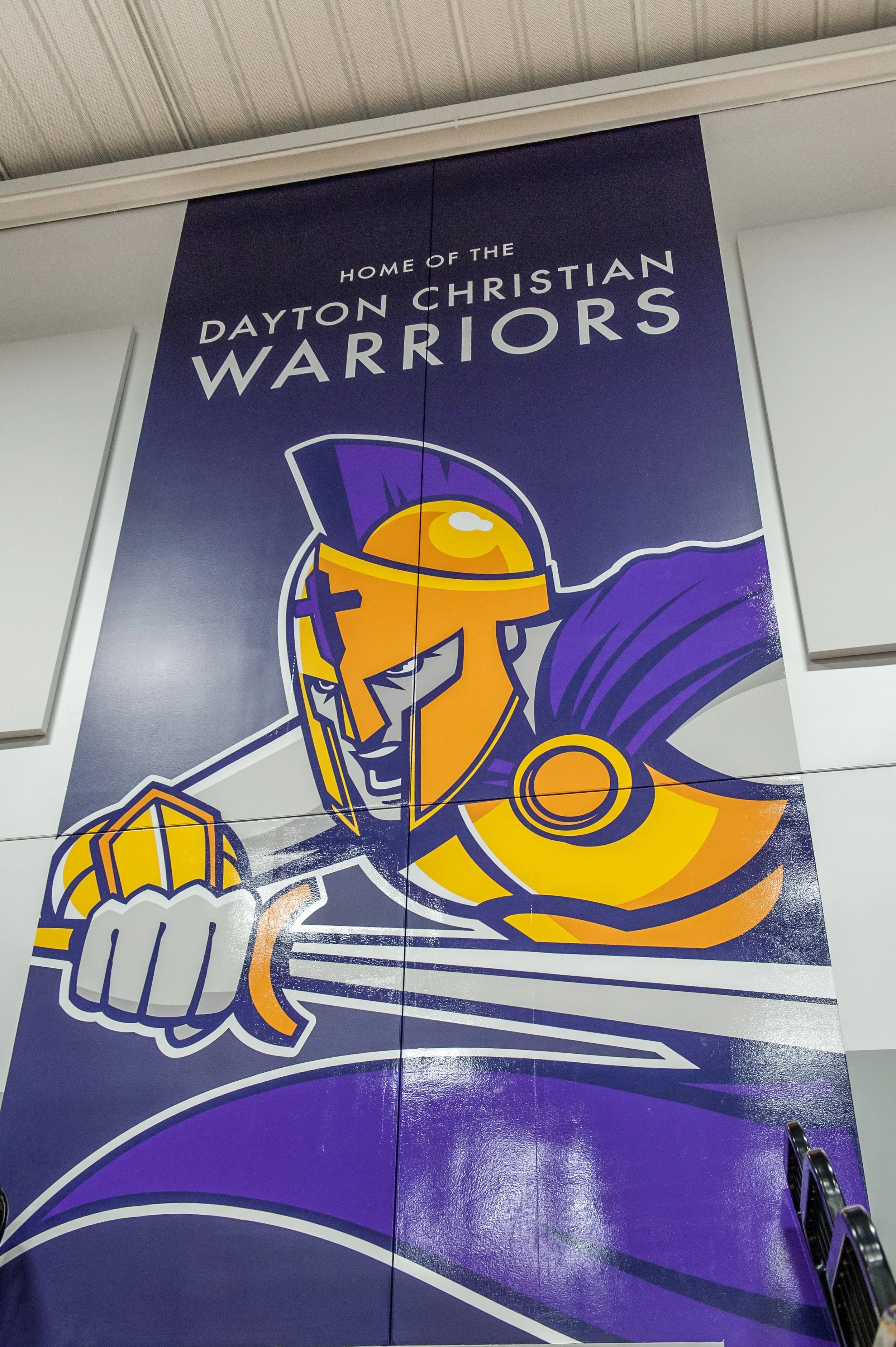 A large banner displaying the Dayton Christian Warriors mascot with the text "Home of the Dayton Christian Warriors." The mascot depicts a warrior in a purple helmet, armor, and cape, holding a shield and a clenched fist.
