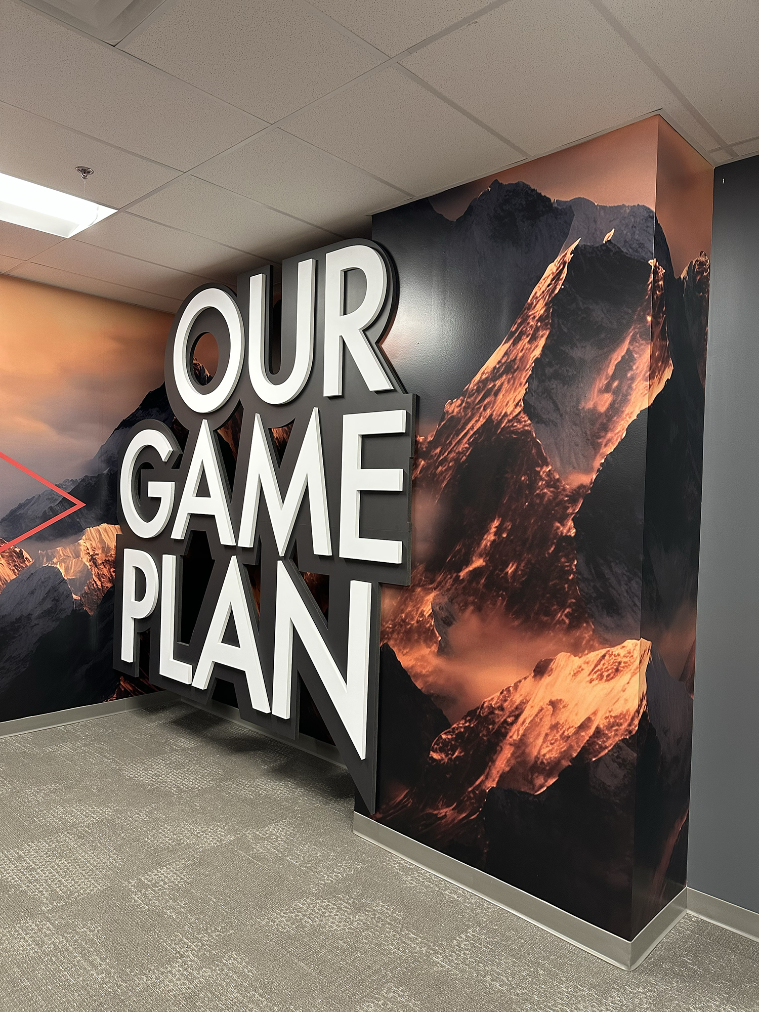 Interior of an office or conference area with a mountain landscape mural on the wall and large 3D white letters spelling 'OUR GAME PLAN'.
