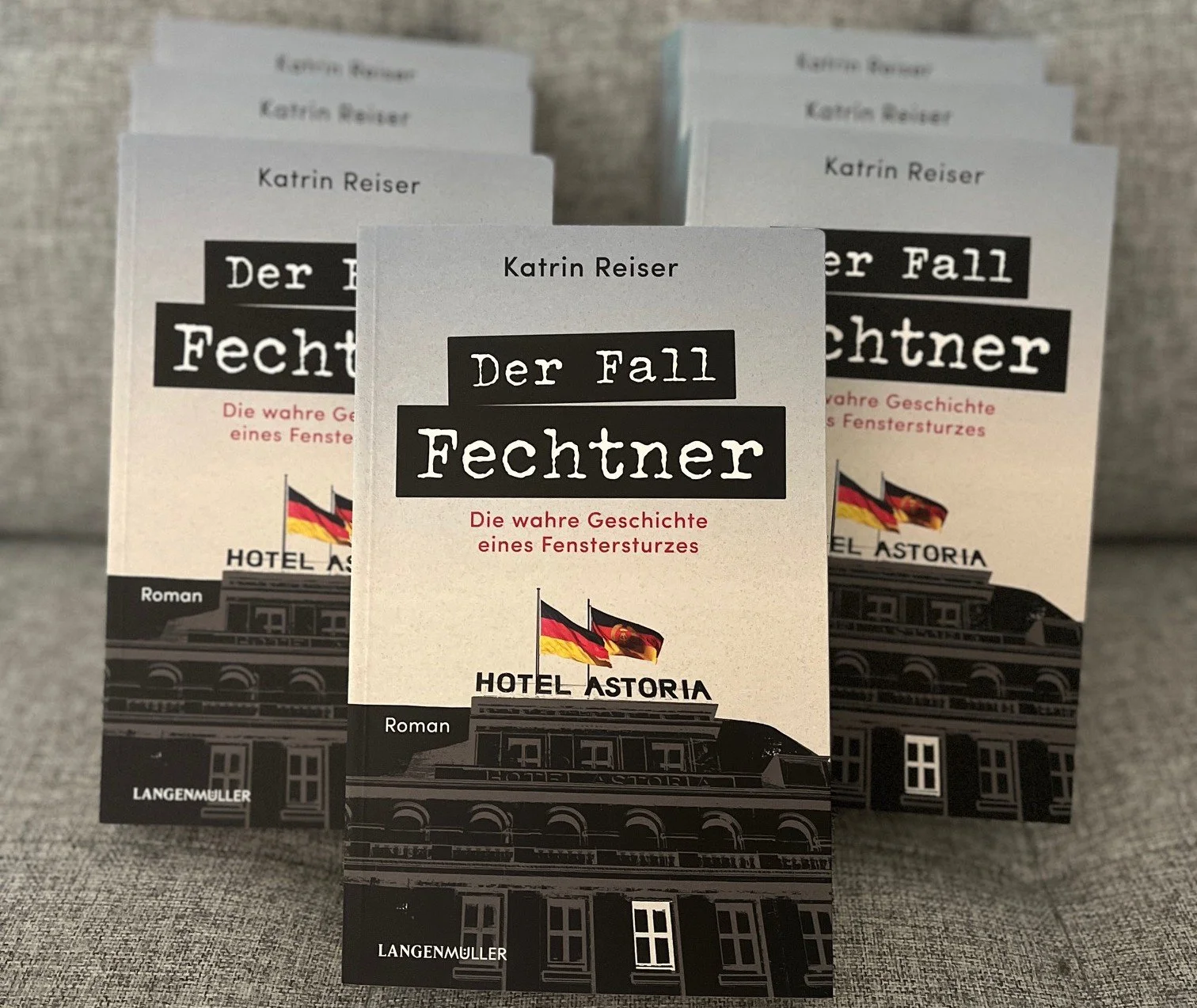 Bücher des Romans "Der Fall Fechtner" von Katrin Reiser, die auf einem Tisch liegen, mit einem Bild des Hotels Astoria mit deutschen Flaggen auf dem Cover.