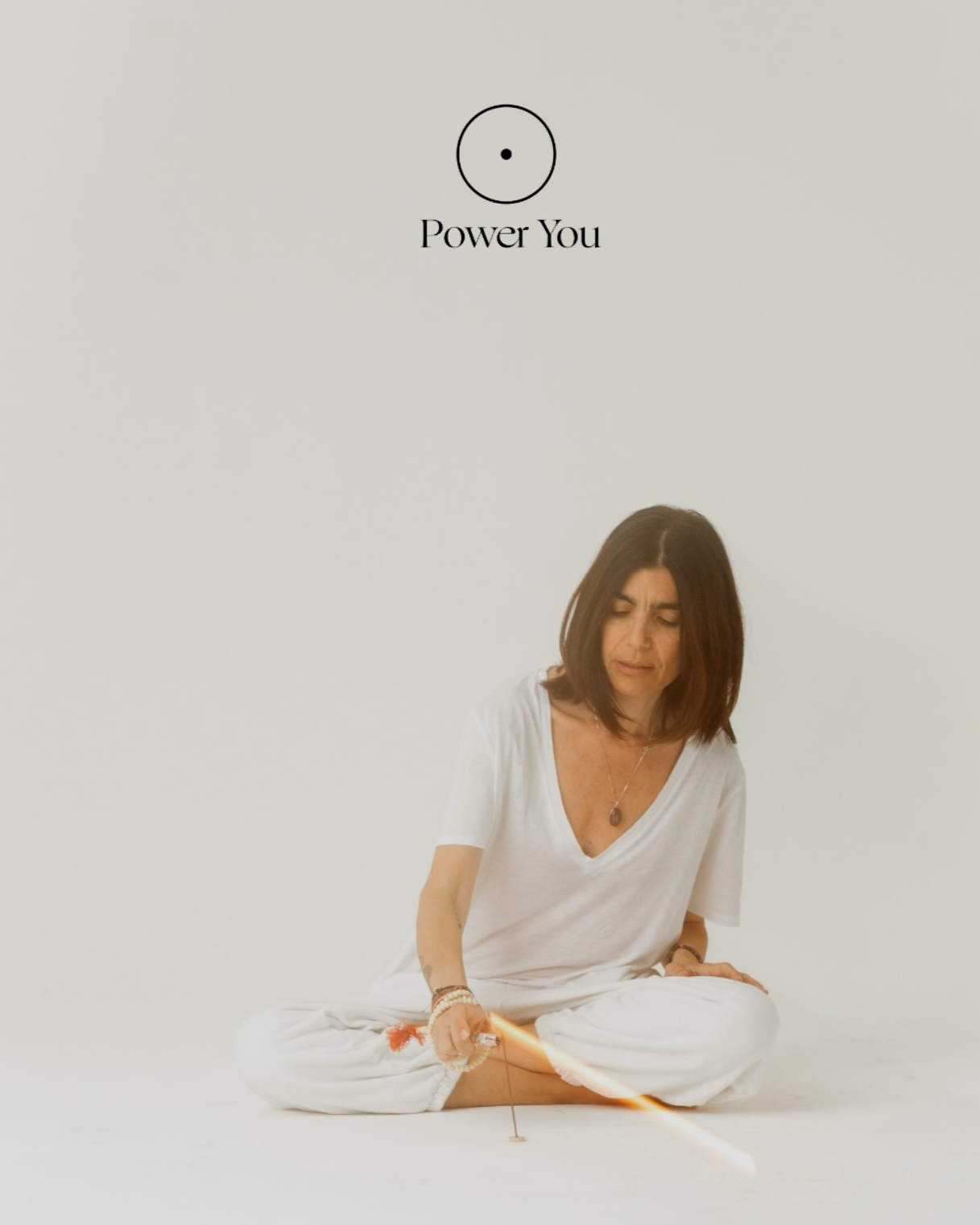 Donna seduta in posizione di meditazione che tiene un bastone con una luce brillante, sfondo bianco, con testo 'Power You' sopra.