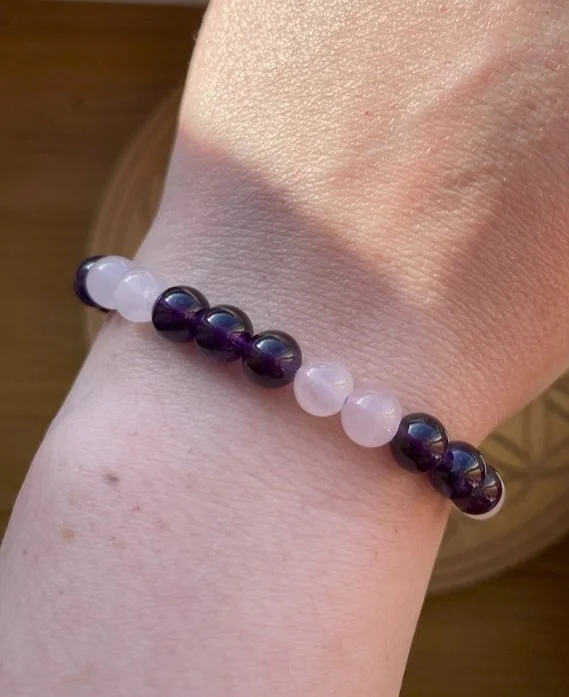 A person's wrist wearing a beaded bracelet with alternating Amethyst and Rose Quartz beads.