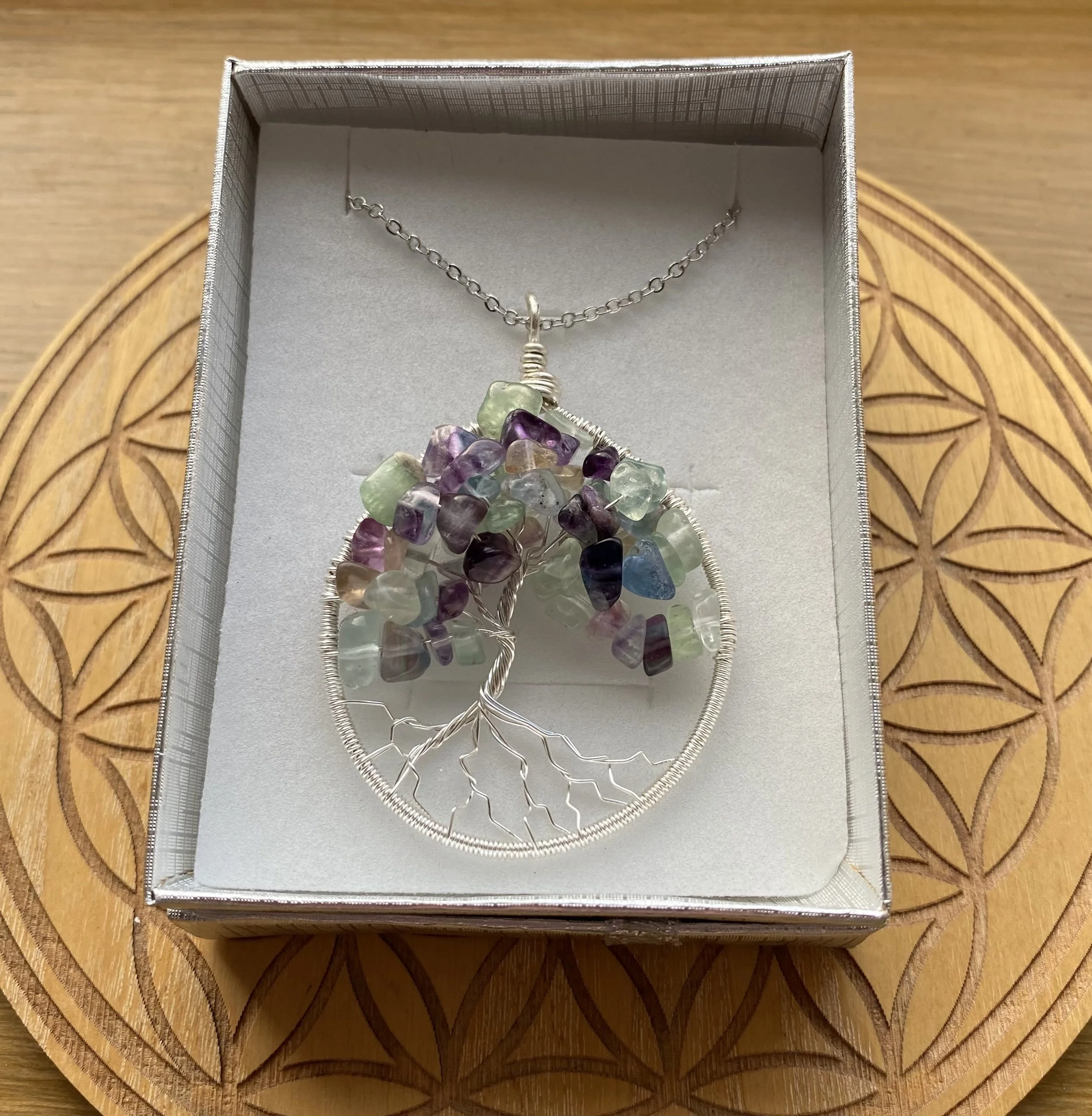 Tree of Life necklace with a pendant made of Fluorite crystal chips in a jewellery box on a wooden surface.