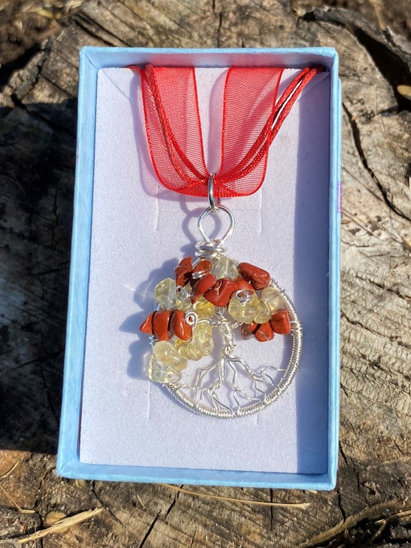 Necklace made with wire, Red Jasper and Citrine crystal chips, designed in the tree of life pattern, placed in a blue jewellery box with a red ribbon, outdoors on a wooden surface.