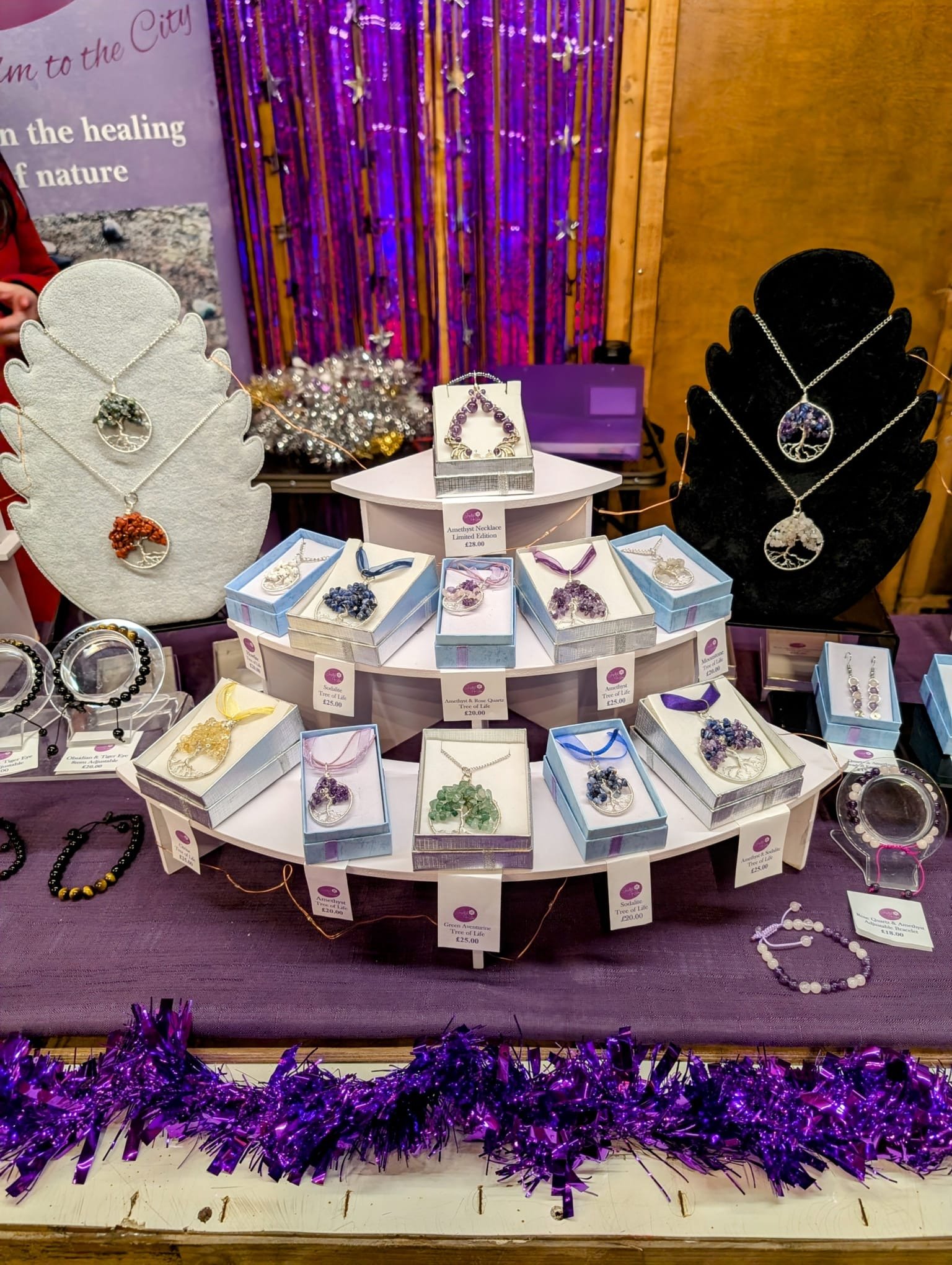 Display of jewelry, including necklaces and earrings, on velvet and cardboard stands at a market stall, with purple tinsel decoration in the foreground.