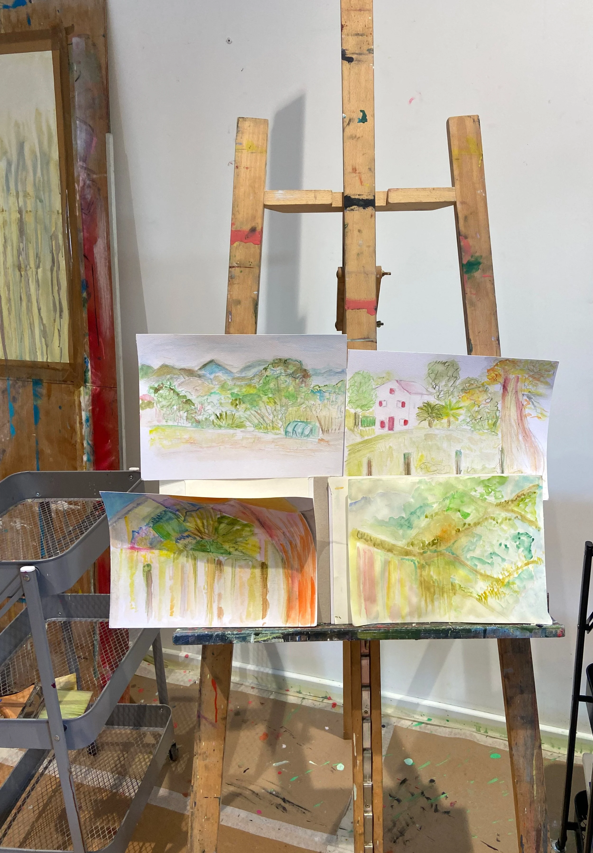 Étude de paysages avec plusieurs peintures en aquarelle représentant des scènes de campagne avec des maisons, des arbres et des montagnes, dans un atelier d'artiste.