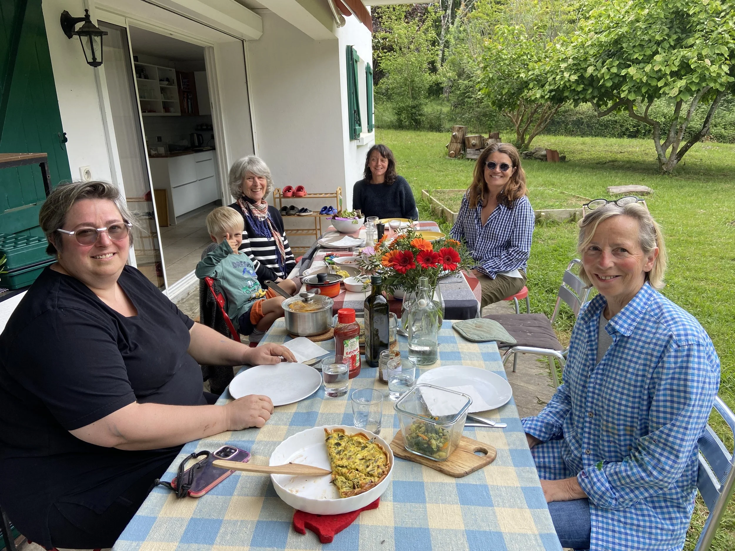 Groupe de personnes assises autour d'une table de pique-nique avec de la nourriture, dans un jardin verdoyant, souriant et profitant du plein air.