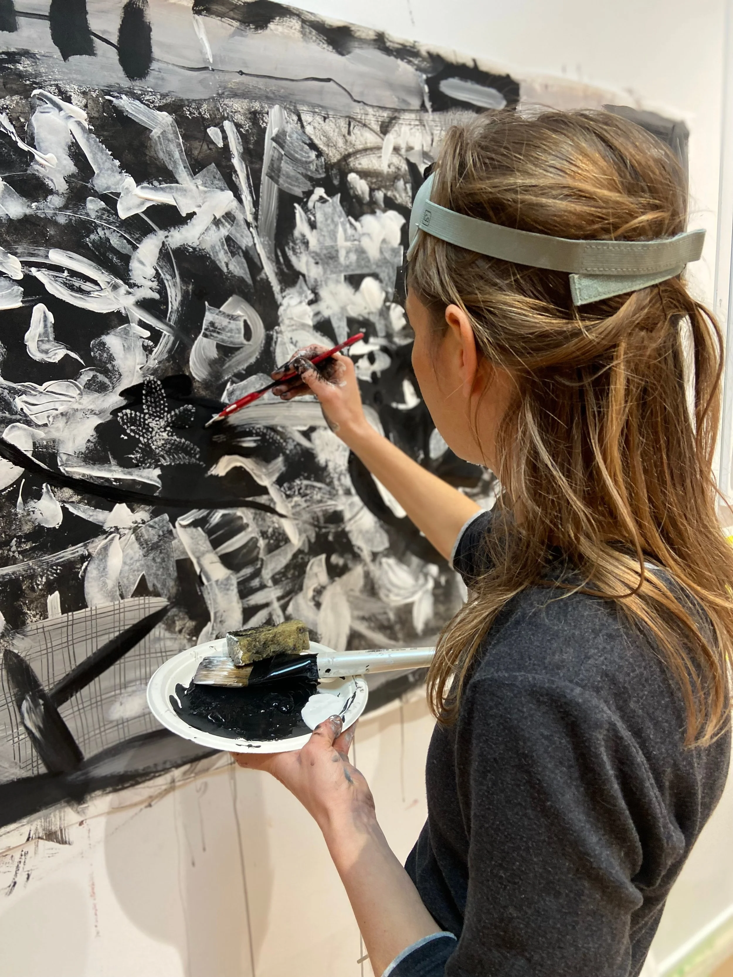 Une femme peint avec de la peinture noire et blanche sur un mur blanc, utilisant un pinceau et un plateau à peinture.
