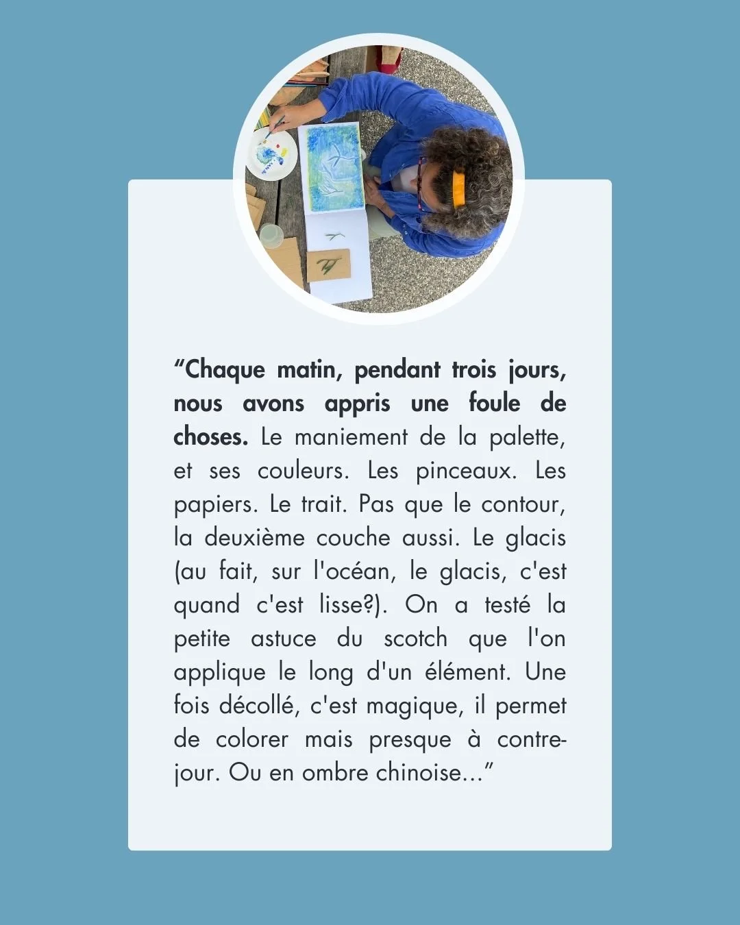 Une personne avec des cheveux gris et une coiffure en queue de cheval, portant un vêtement bleu, est assise à une table en train de peindre ou d'étudier des images et des matériaux artistiques. La photo est prise d'en haut, dans un cadre extérieur.