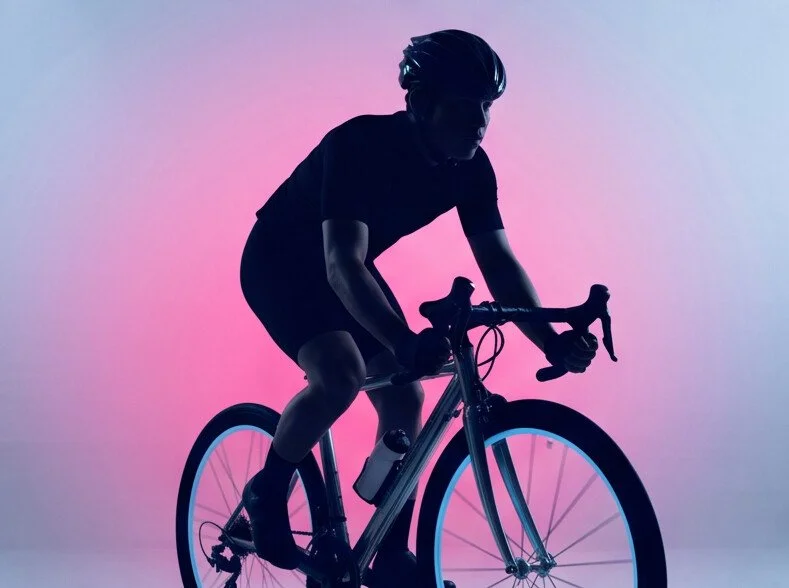 Persona en Silueta montando bicicleta en fondo con iluminación rosa y azul.