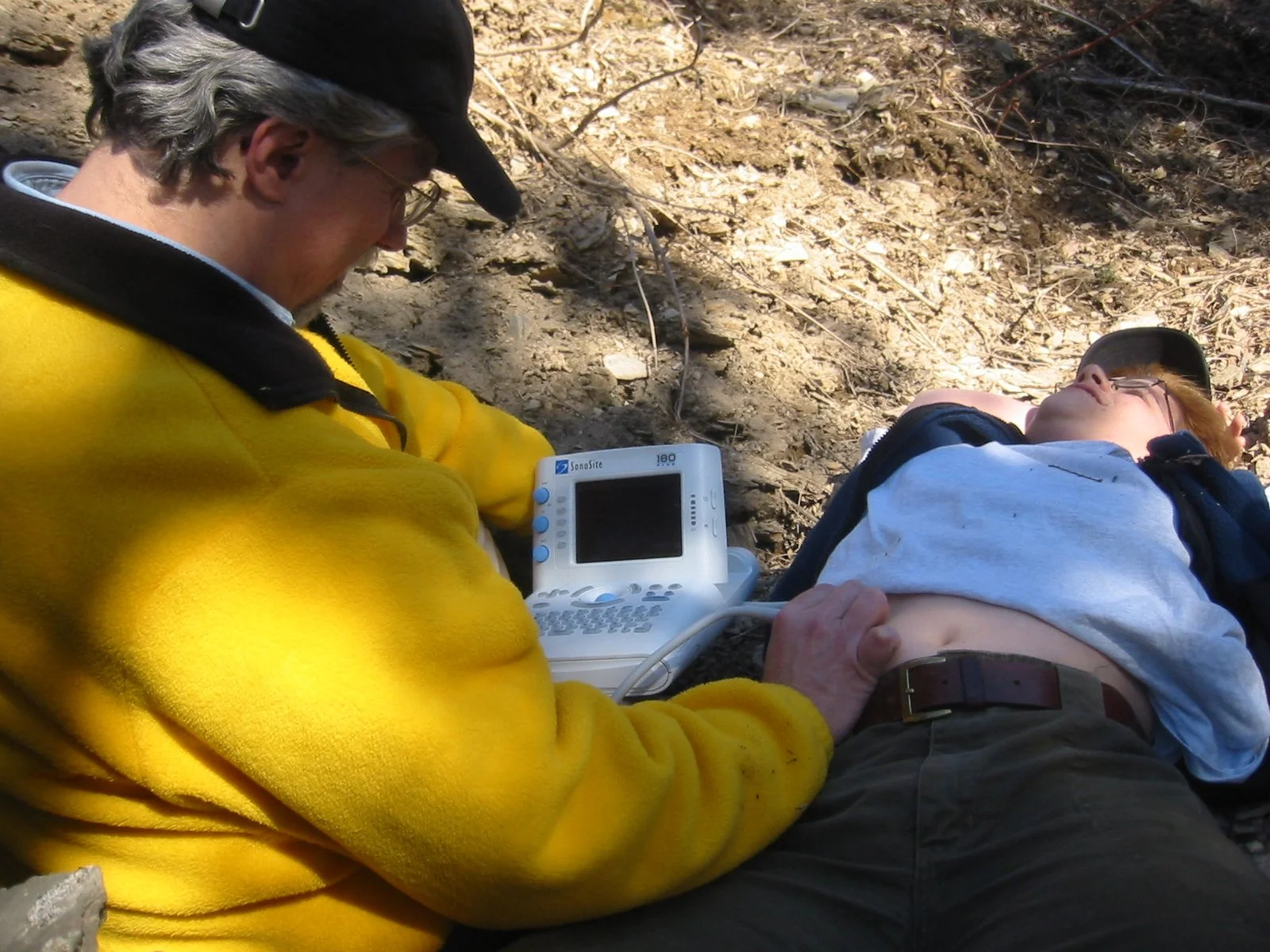 A rescuer performs a point of care ultrasound on a wilderness patient lying on the ground.