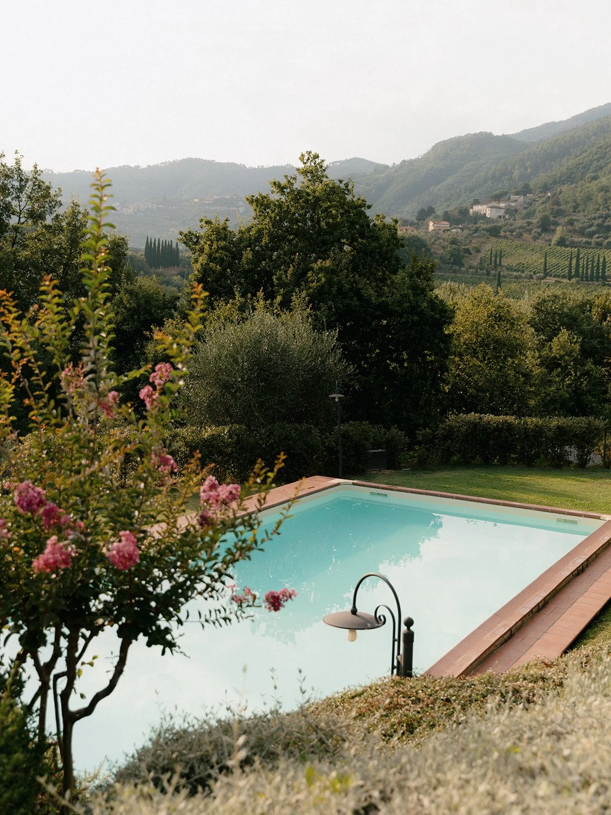 Outdoor swimming pool with surrounding garden and hills in the background.
